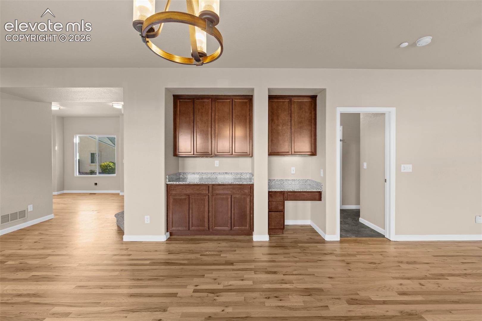 Built-in cabinetry with natural wood finish, stone-surfaced countertops, integrated workstation, wood-finish flooring, and circular tiered chandelier