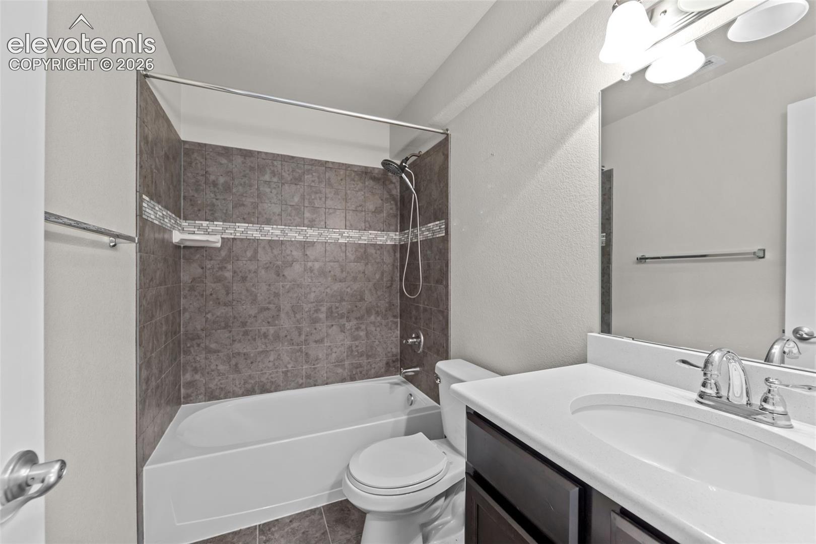 Bathroom featuring a white vanity with integrated sink, dark wood-finish cabinetry, a chrome faucet, and a shower/tub combination with tiled surround and decorative accent band