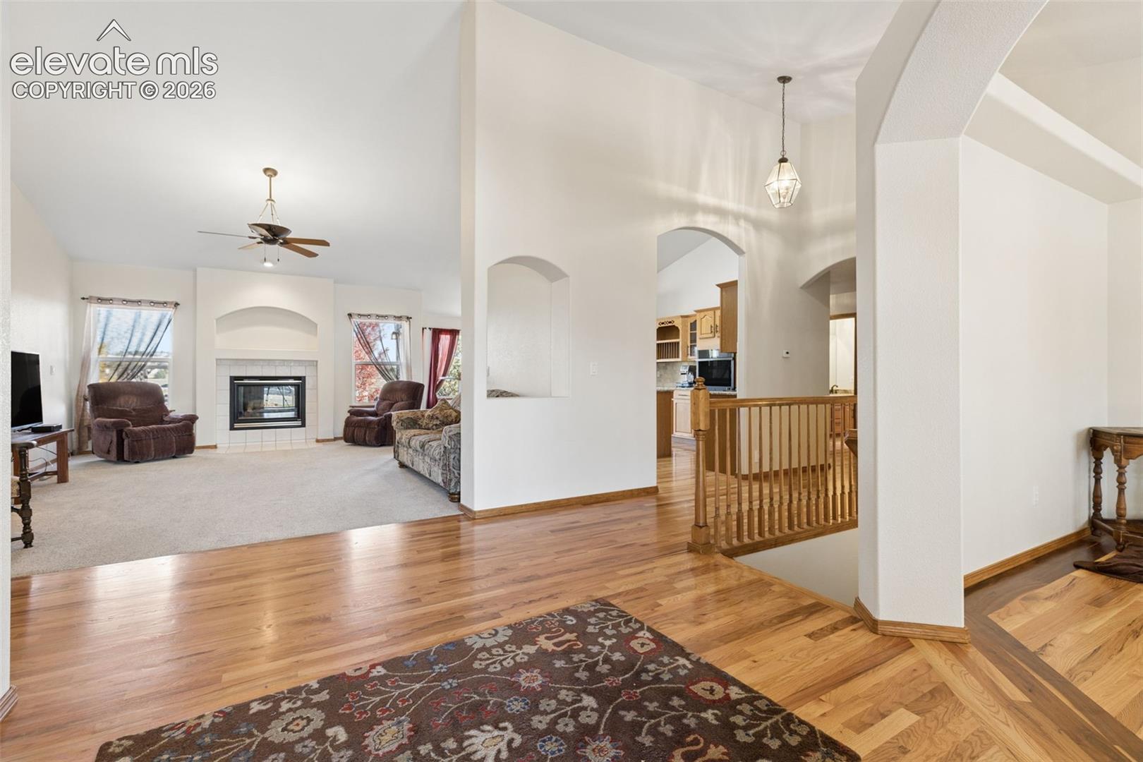Open-concept interior featuring wood-finish flooring, a fireplace with a decorative arched niche, vaulted ceilings, and a wooden stair railing