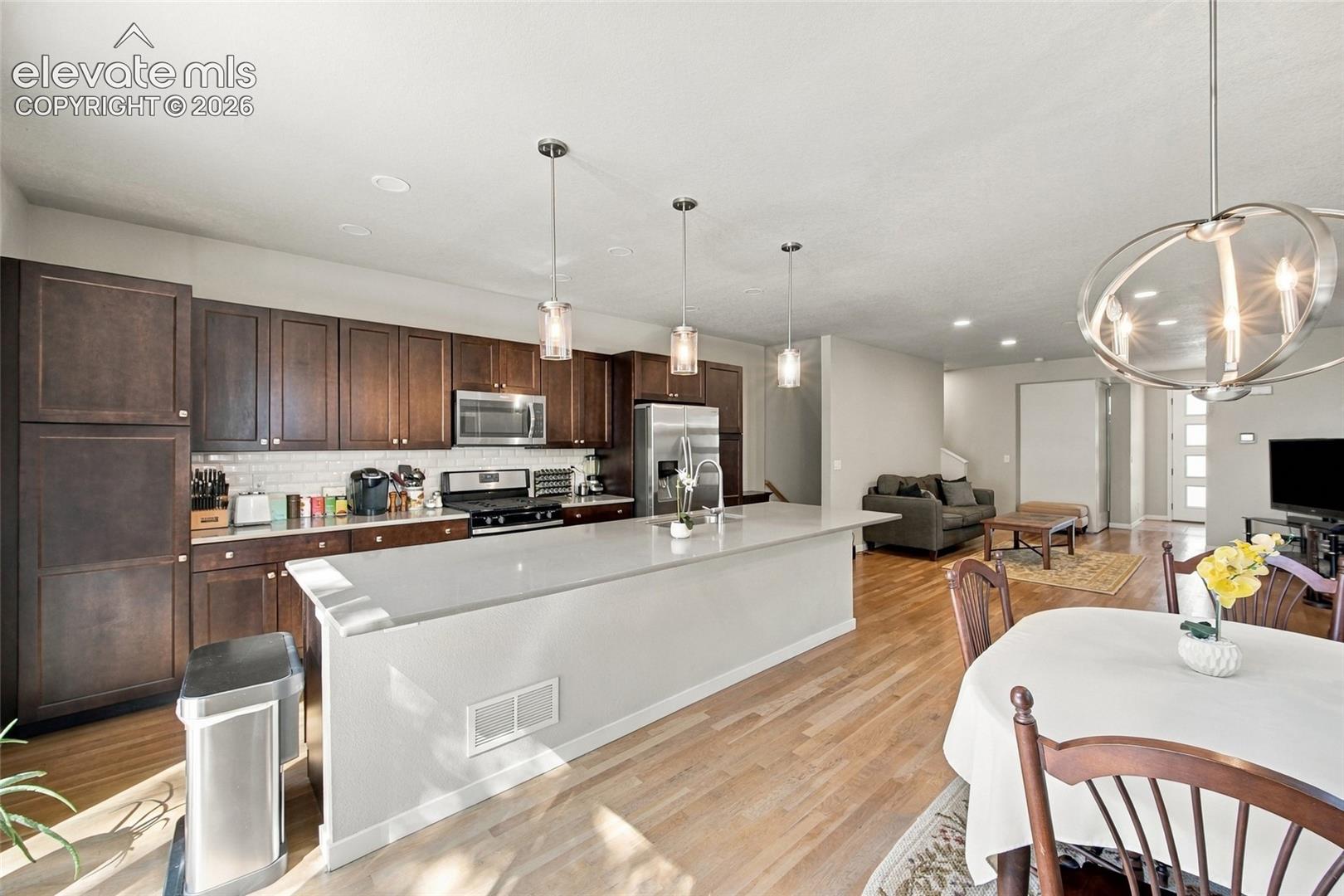 Kitchen featuring dark cabinetry, quartz-topped island, wood flooring, stainless steel appliances, and pendant lighting
