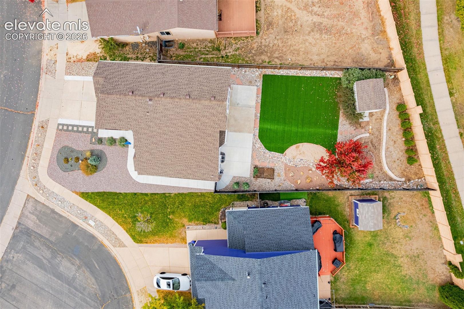 Aerial view of property featuring a low-maintenance artificial turf lawn, decorative rock landscaping, a concrete driveway, and a detached storage structure