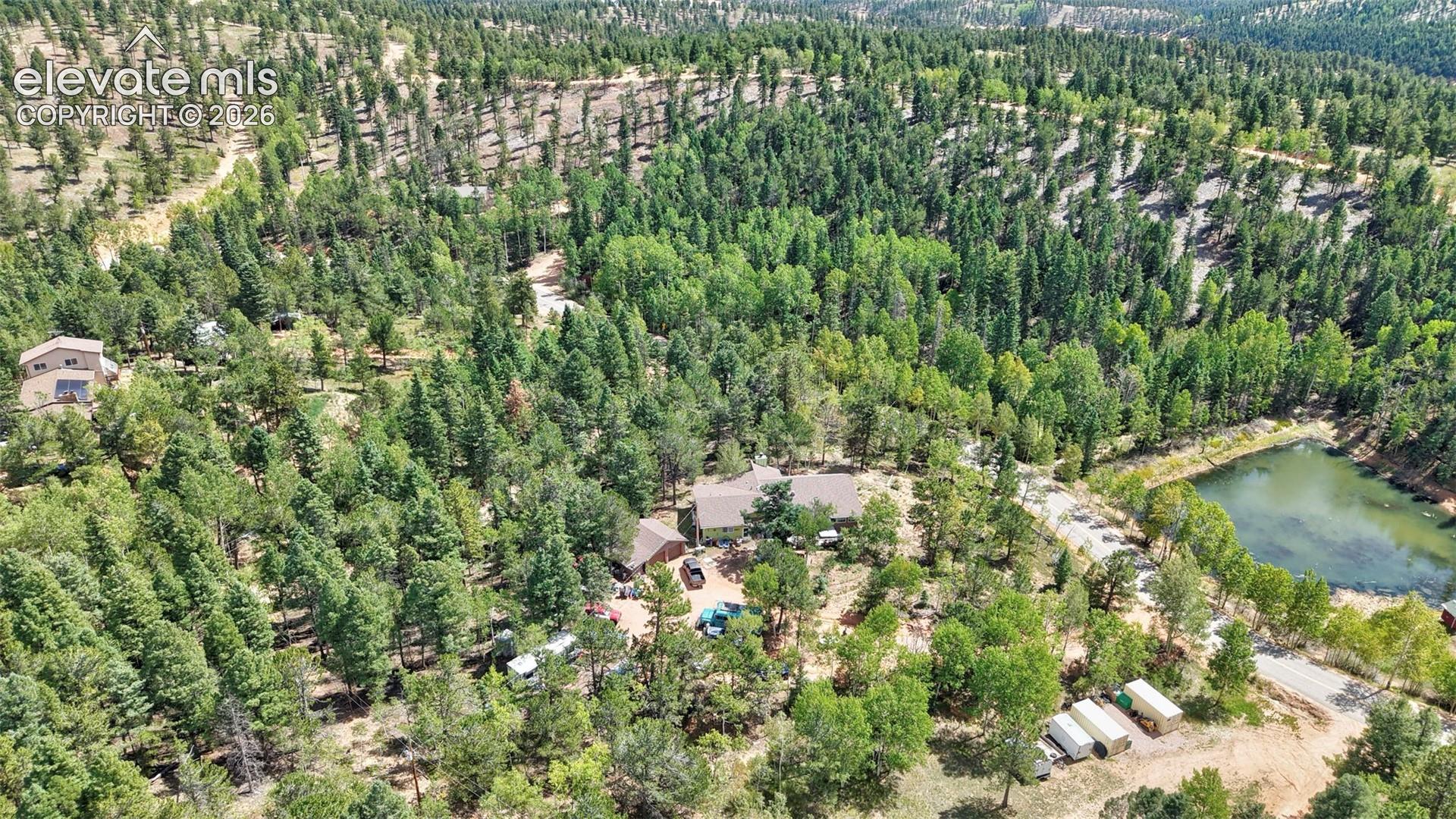 Extensive tree coverage surrounding multiple structures, with a body of water prominently featured