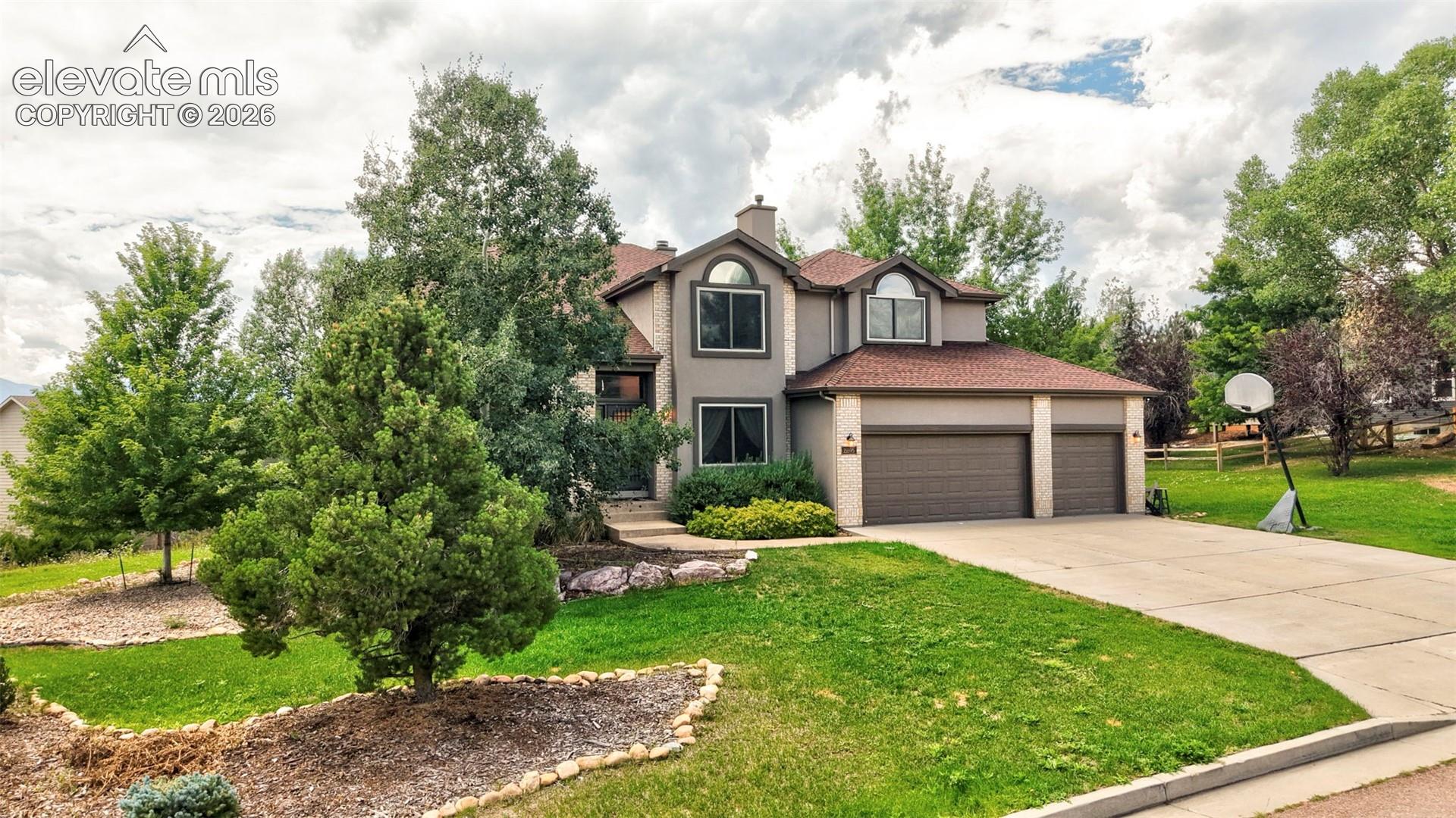 Two-story residence with a three-car garage, concrete driveway, and a front yard featuring mature trees and landscaped beds