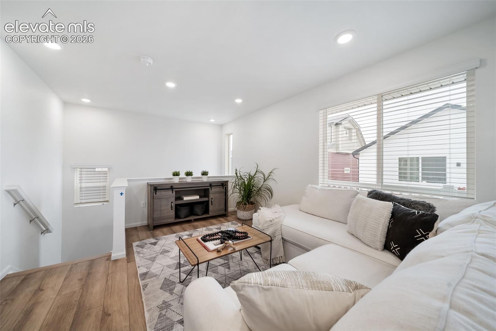 Recessed lighting, wood-finish flooring, white walls, large window with blinds, and a built-in media console
