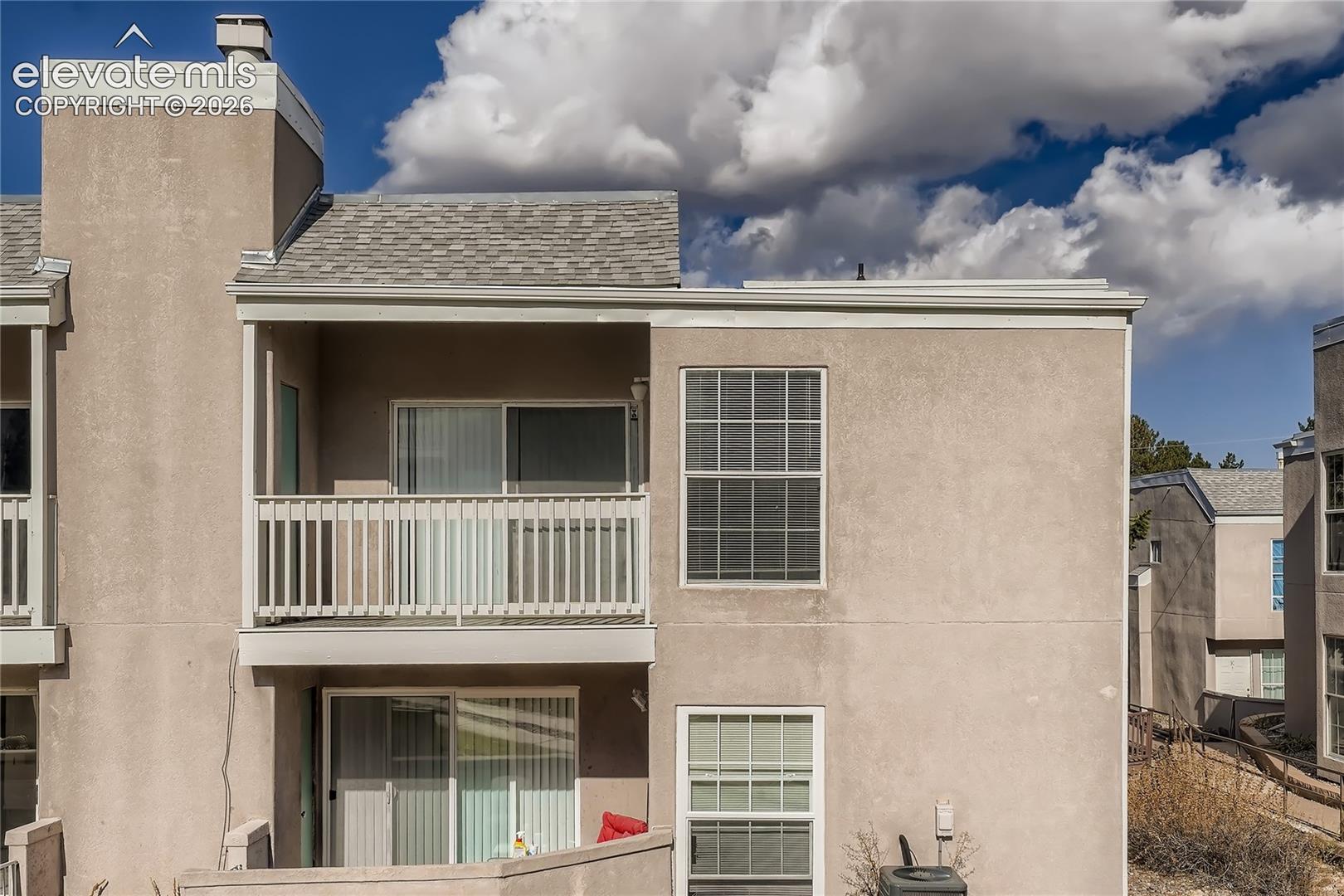 Stucco exterior featuring a second-story balcony with white railing, sliding glass doors, and asphalt shingle roofing