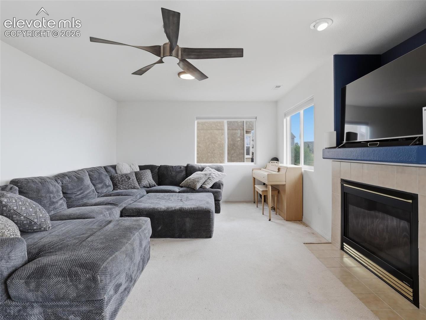 Living space featuring a tiled fireplace with a black insert, an integrated media niche, dual windows, and a ceiling fan with integrated lighting