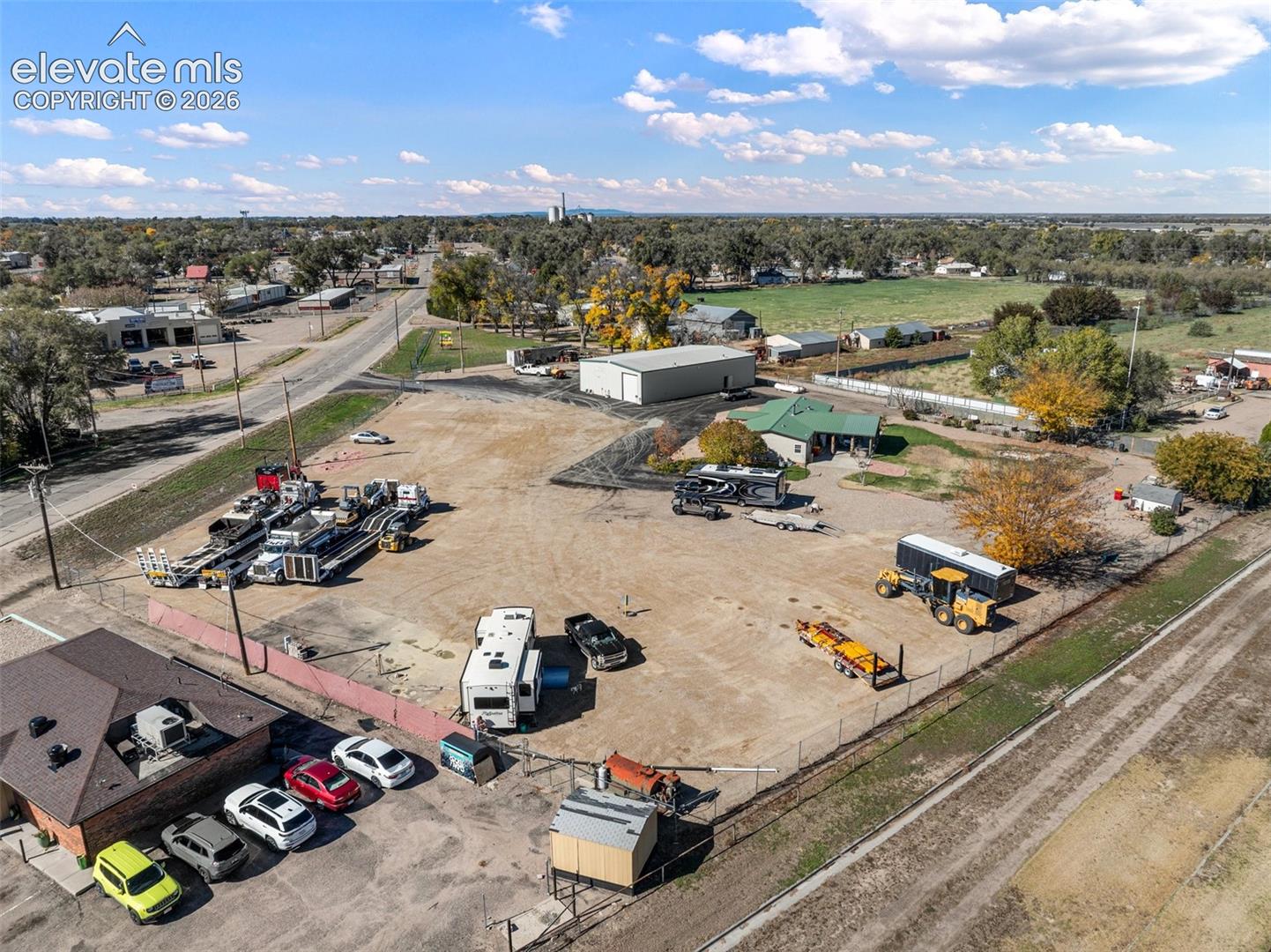Expansive lot featuring a large metal-sided outbuilding, partial perimeter fencing, and dual-access points via paved and unpaved surfaces