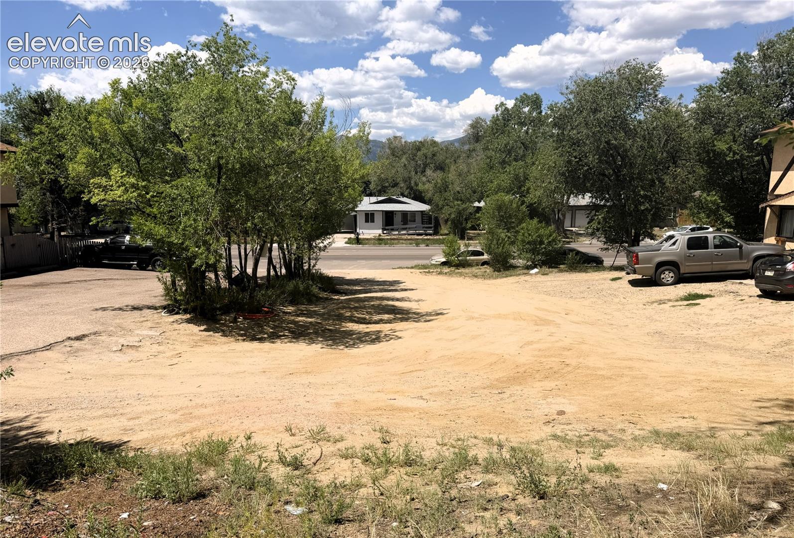 Expansive gravel lot with surrounding mature trees and partial mountain backdrop