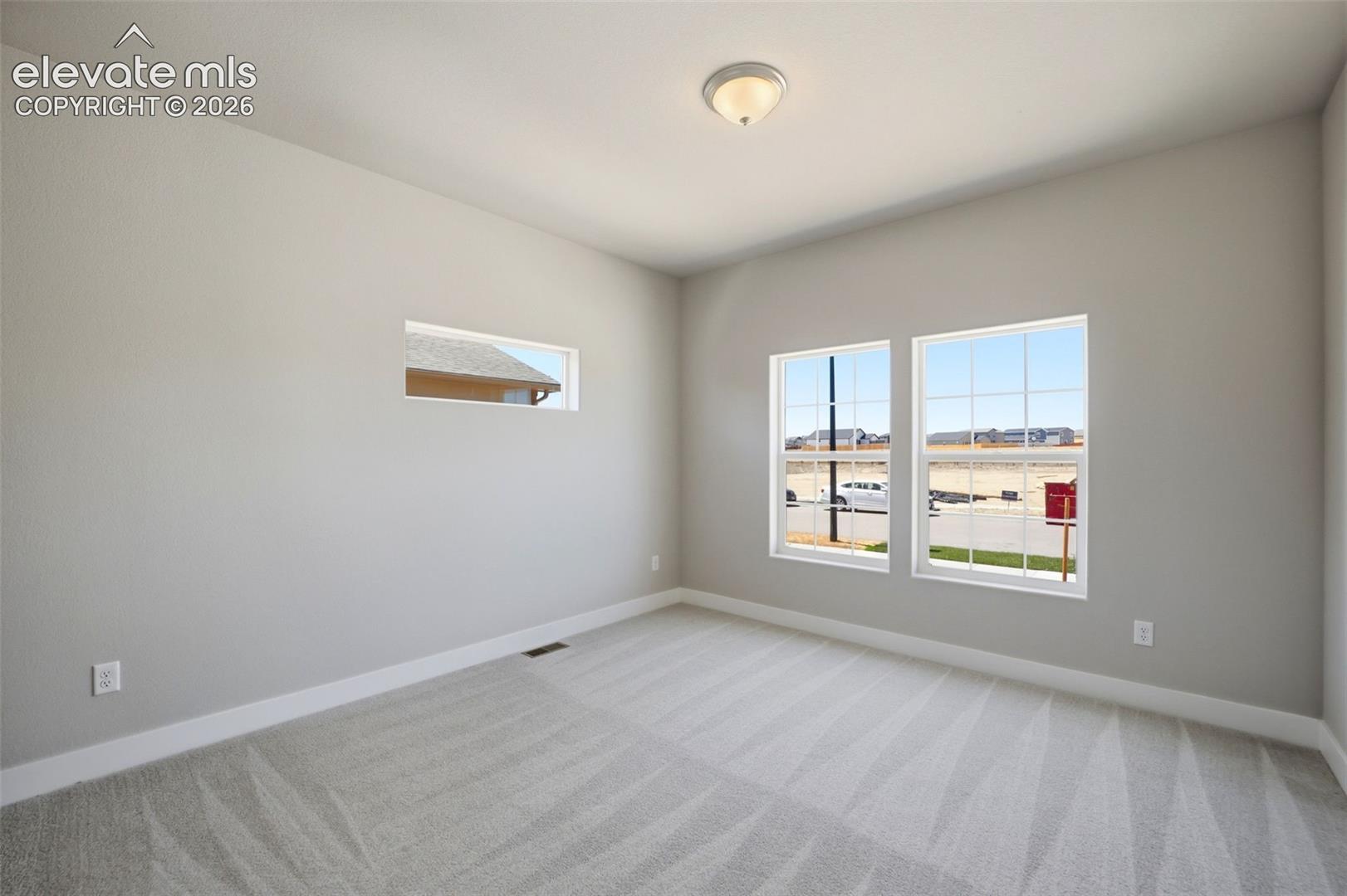 Neutral-toned room featuring neutral carpeting, double-pane windows with muntins, a horizontal accent window, and a flush-mount light fixture