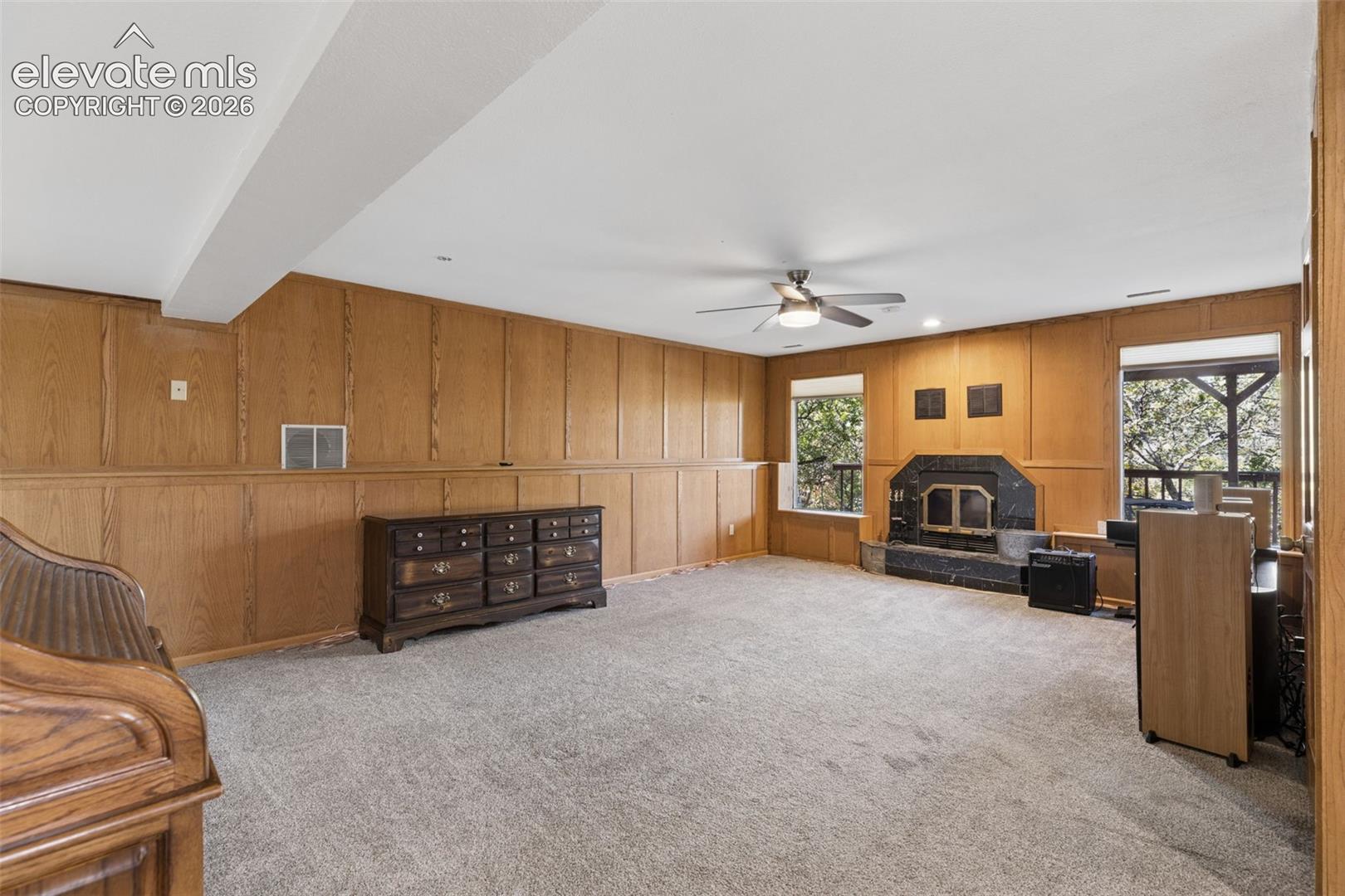 Paneled wood wall detailing, stone fireplace surround, inset hearth, and ceiling fan with integrated lighting