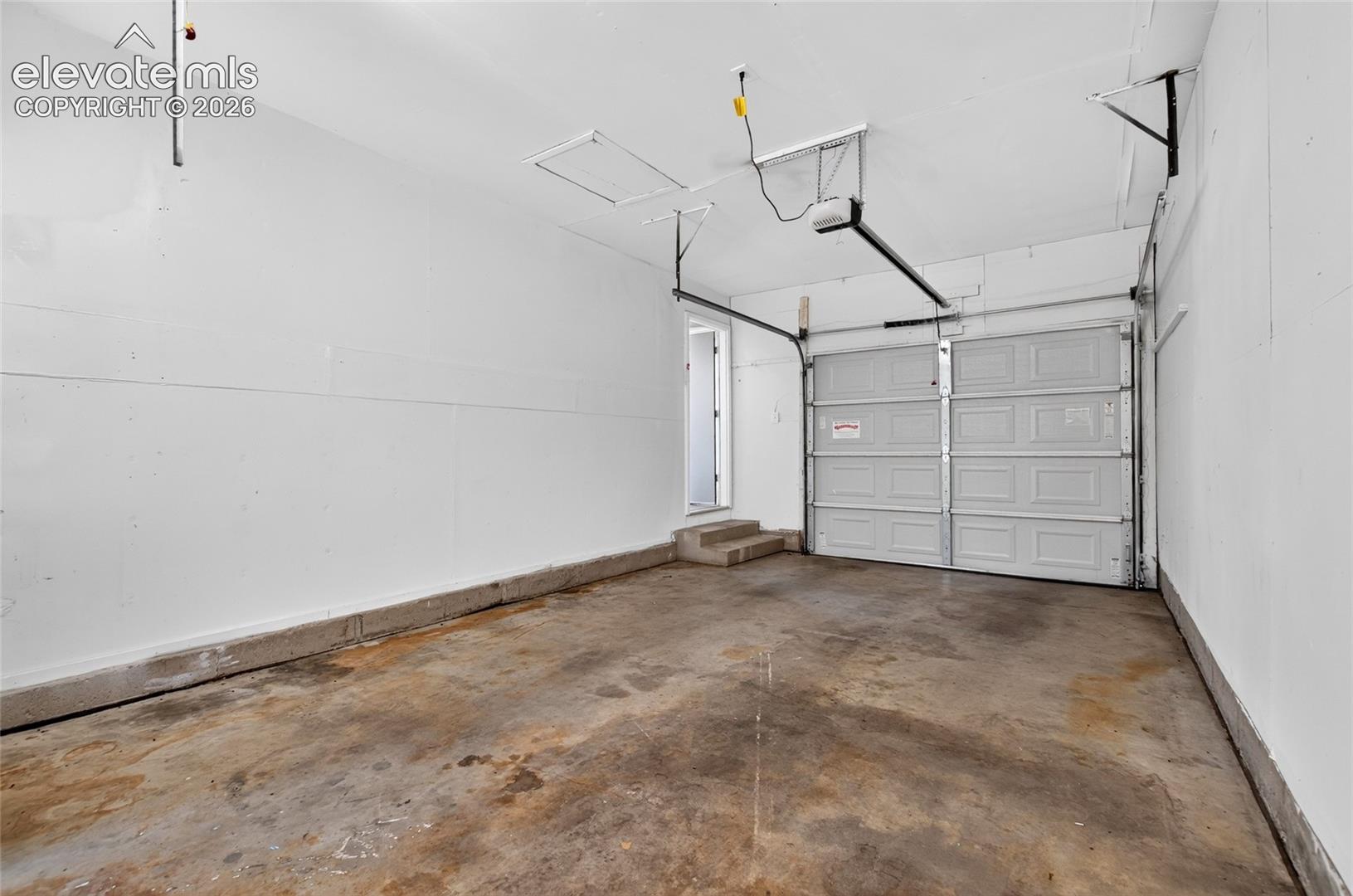 Spacious garage featuring a concrete floor, white walls, and a paneled garage door