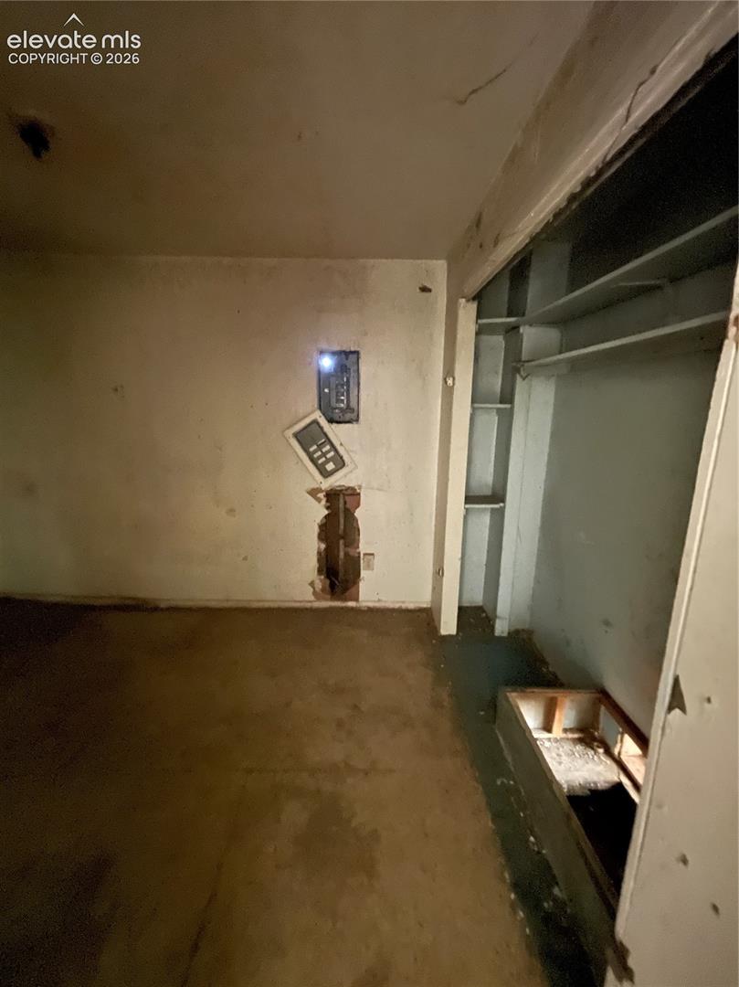 Built-in closet featuring tiered shelving and a recessed storage compartment, electrical panel with access door, and wall-mounted electrical components