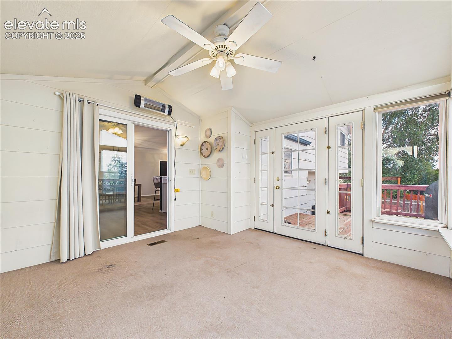 Sun-filled enclosed sunroom with vaulted ceiling, large picture windows, and direct access to the spacious backyard deck for seamless indoor-outdoor living.