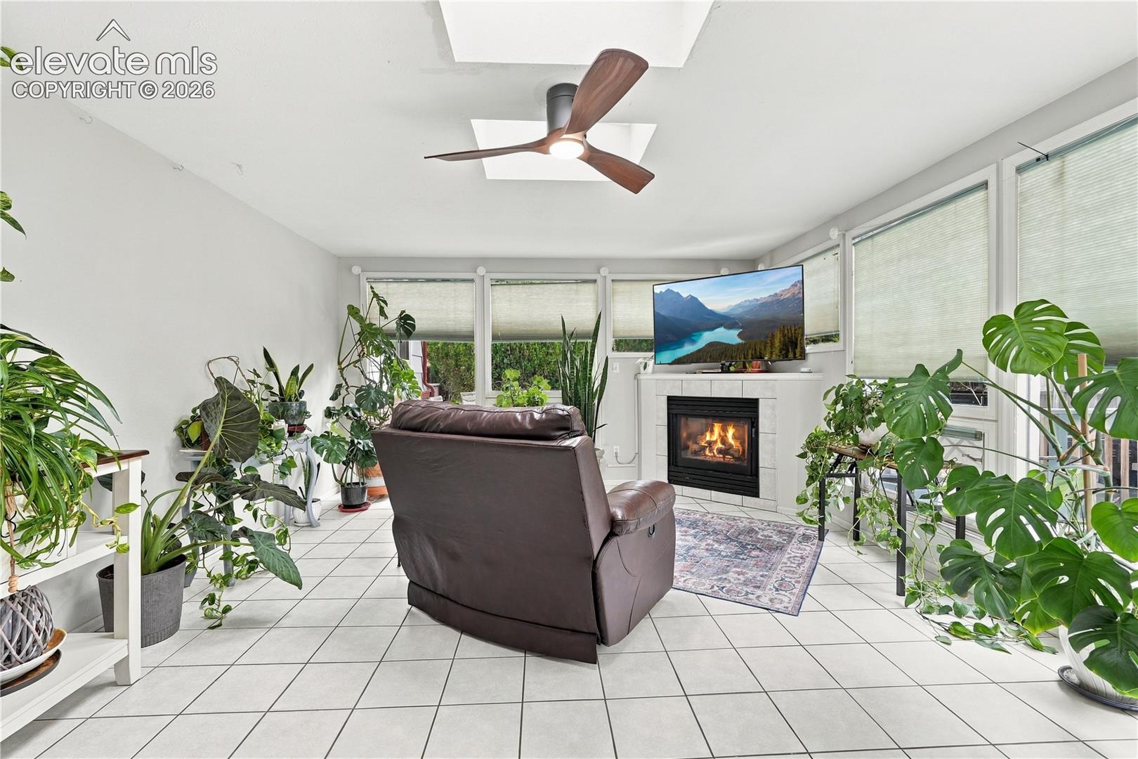Sunroom featuring tile flooring, a fireplace with a ceramic tile surround, integrated skylights, and a modern ceiling fan