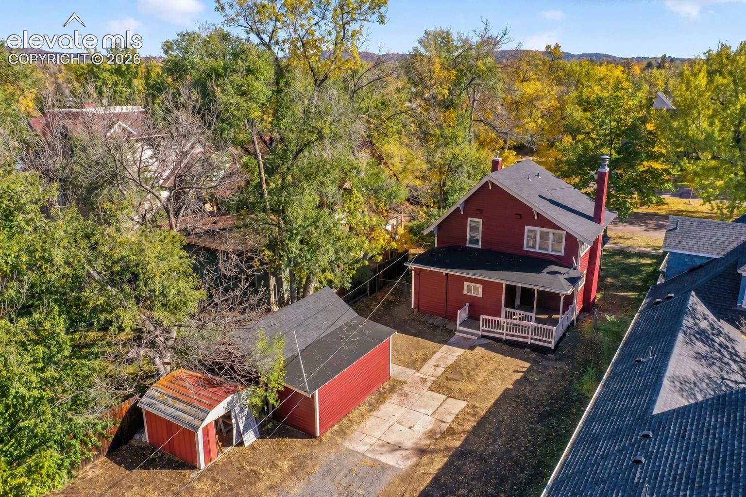 Two-story residence with red siding, detached multi-bay garage, secondary storage structure, covered rear porch, and concrete driveway
