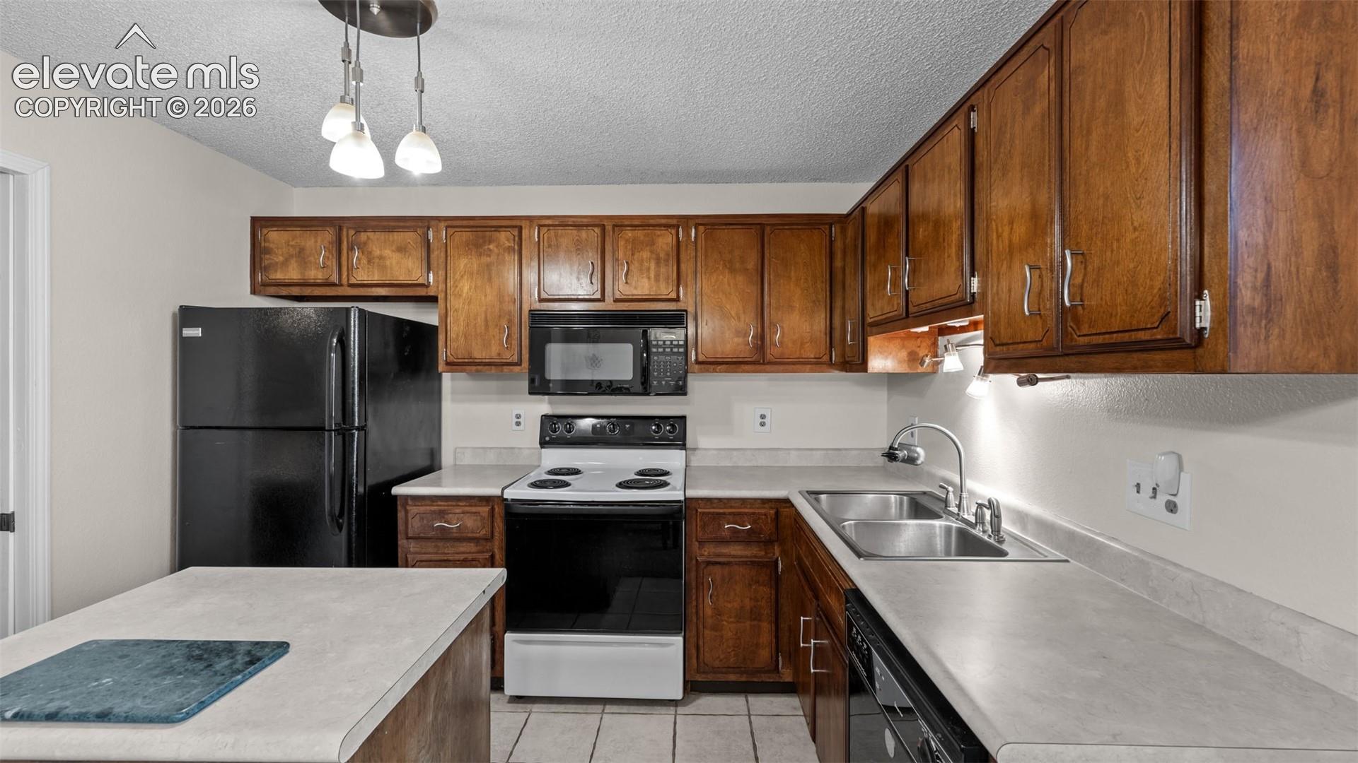 Kitchen featuring stained wood cabinetry, solid surface countertops, a stainless steel double-basin sink with a gooseneck faucet, tile flooring, and a multi-light pendant fixture
