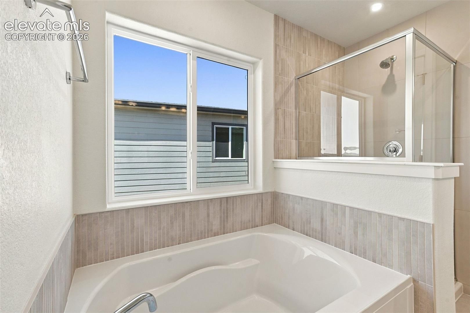 Soaking tub with chrome fixtures, tiled wainscoting, and an adjacent glass-enclosed shower with a rainfall showerhead