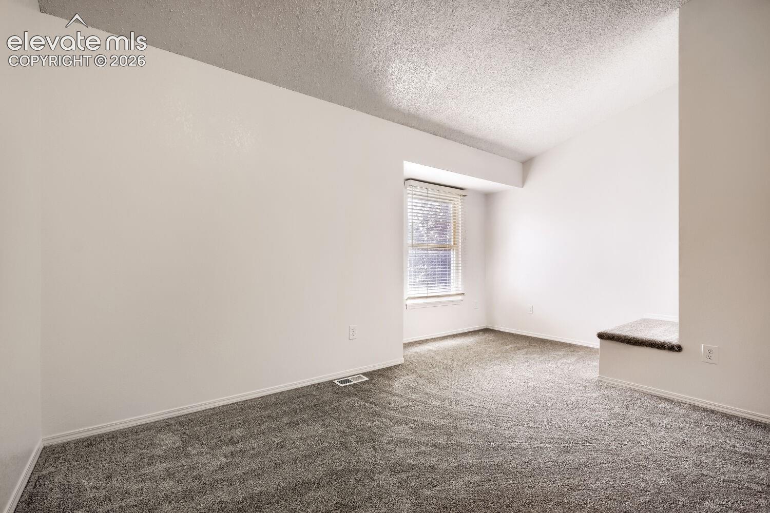 Room featuring a vaulted ceiling, neutral wall finish, carpeted flooring, window with integrated blinds, and a built-in platform