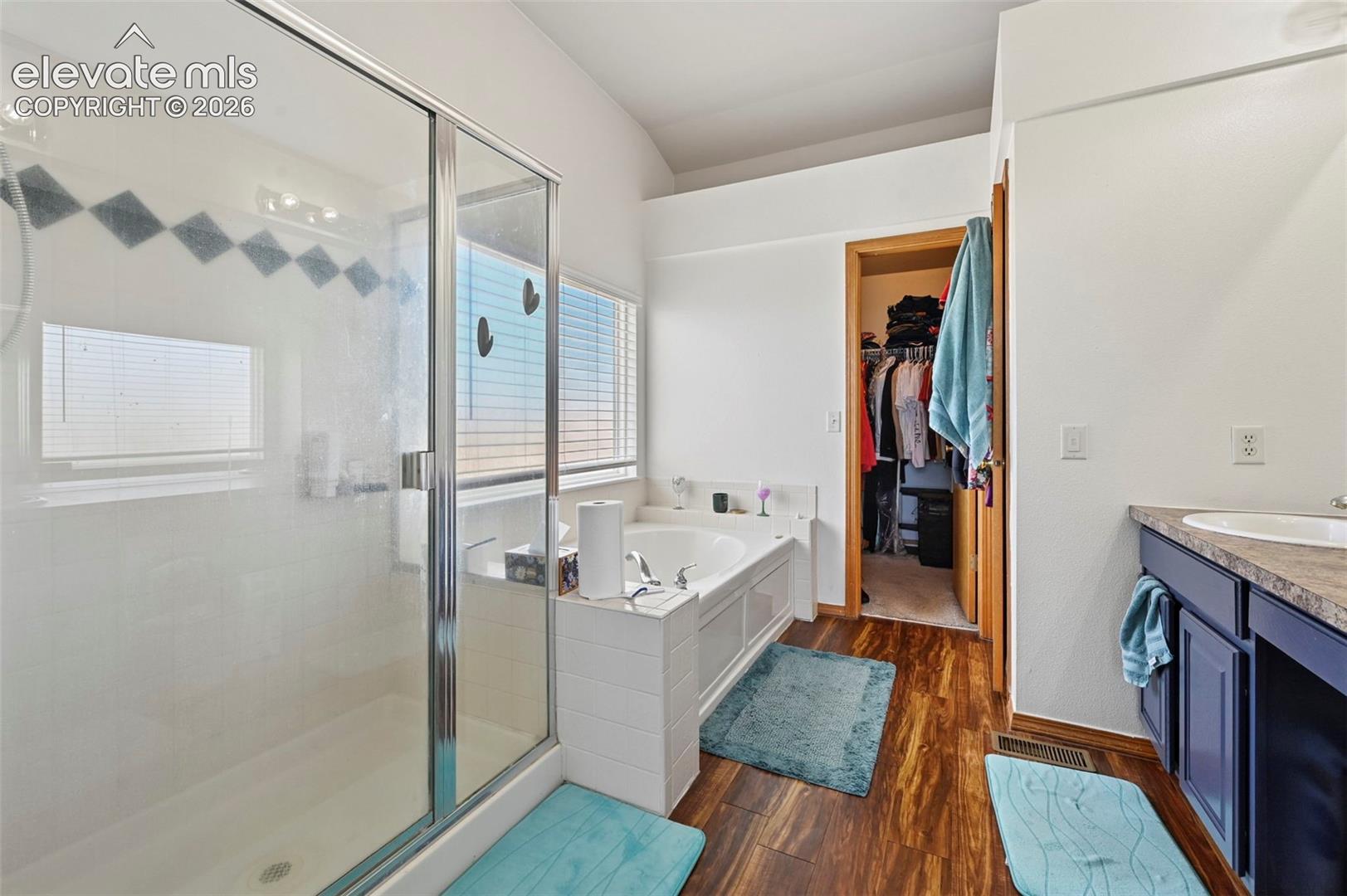 Wood-finish flooring throughout, featuring a glass-enclosed shower, built-in soaking tub, and a vanity with an integrated sink