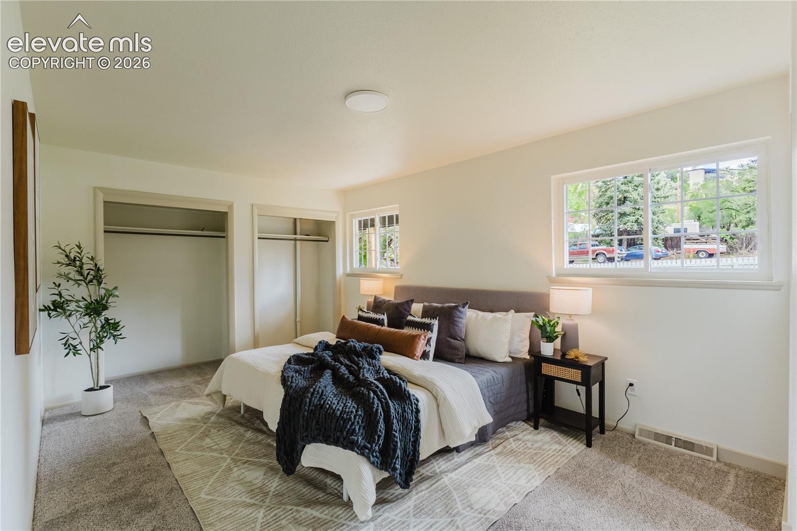 Bright bedroom featuring neutral-toned carpet, white walls, and a large window with white trim