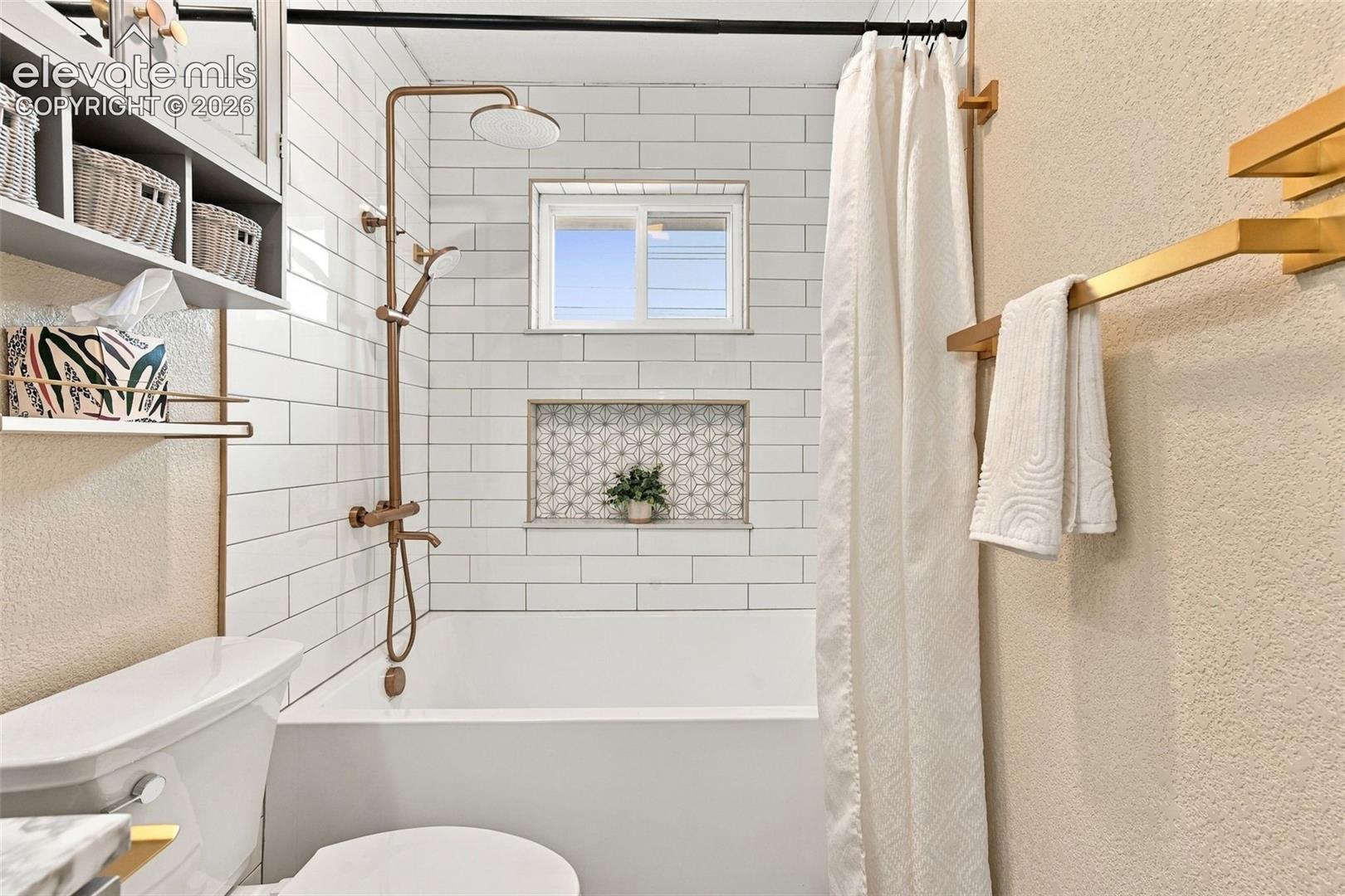 White subway tile shower surround featuring a built-in recessed niche with decorative patterned tile, a dual-head shower fixture in a metallic finish, and a wall-mounted storage cabinet