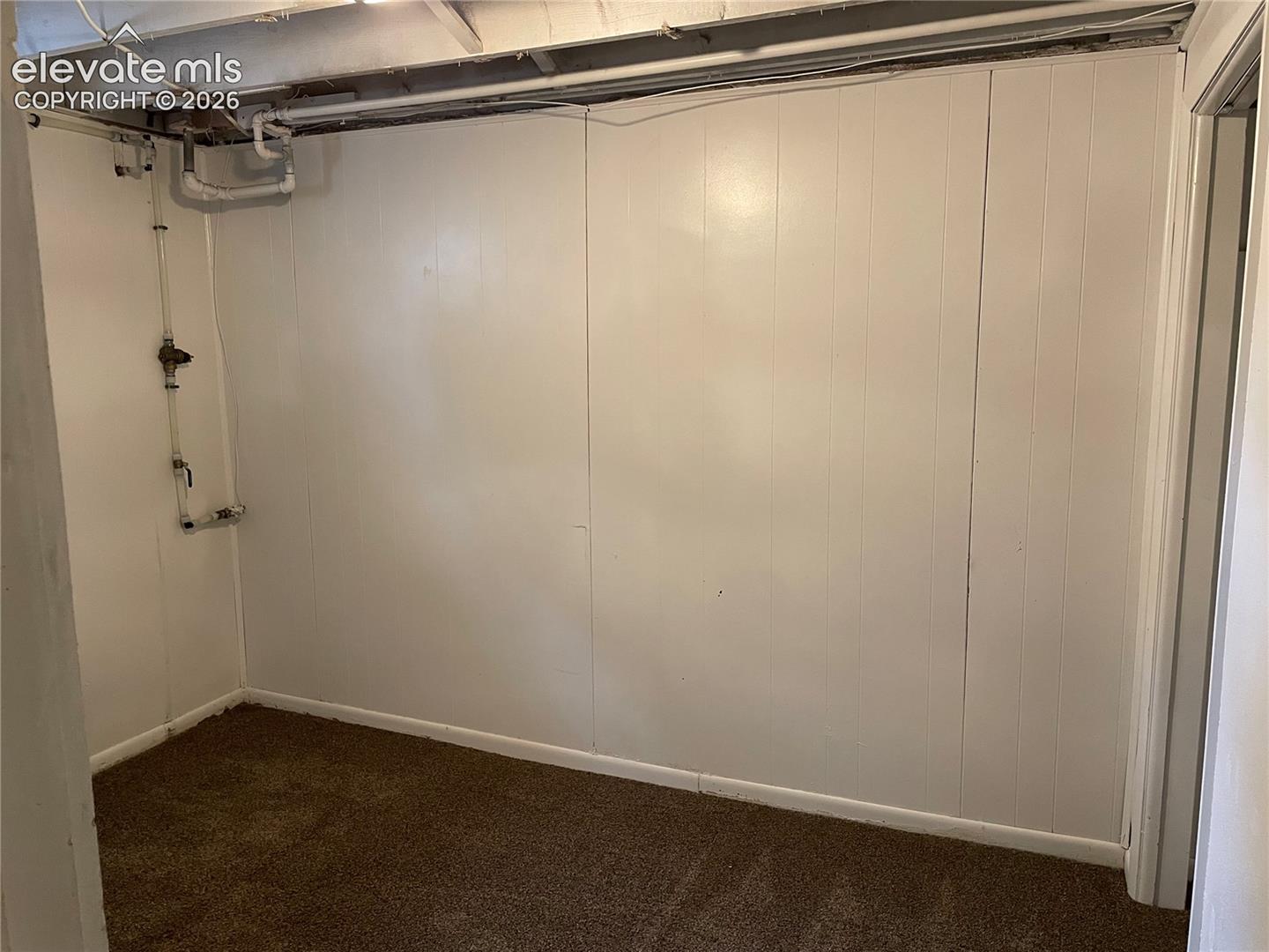 Interior space featuring white vertical paneling and brown carpet flooring