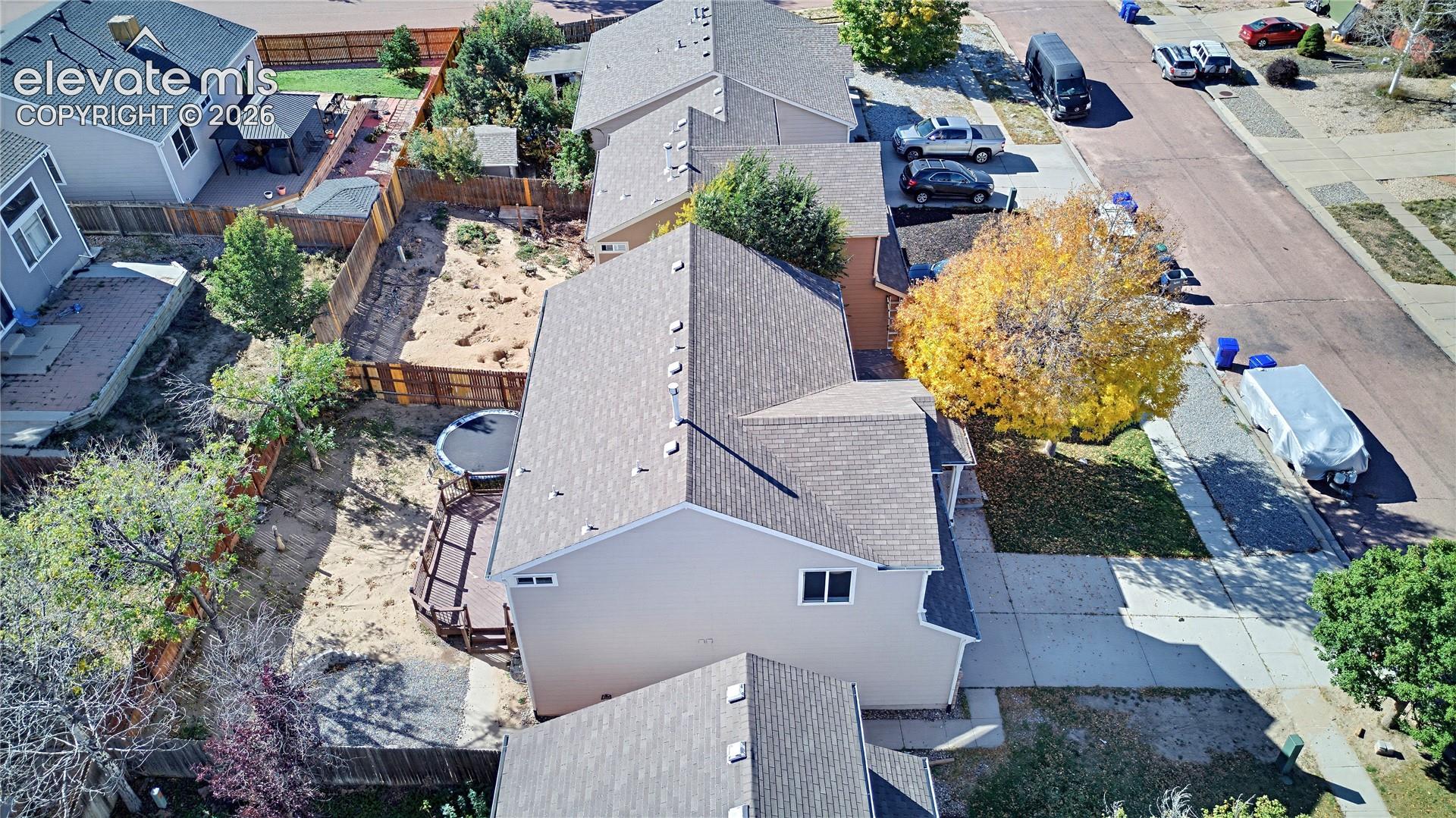 Aerial view featuring a two-story residence, asphalt shingle roofing, wooden deck, fenced perimeter, and driveway