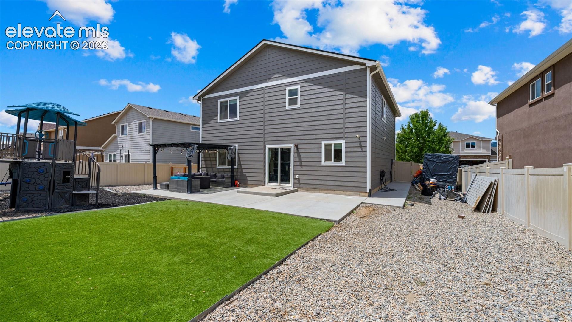 Rear exterior showcasing gray siding with white trim, a concrete patio, and a sliding glass door