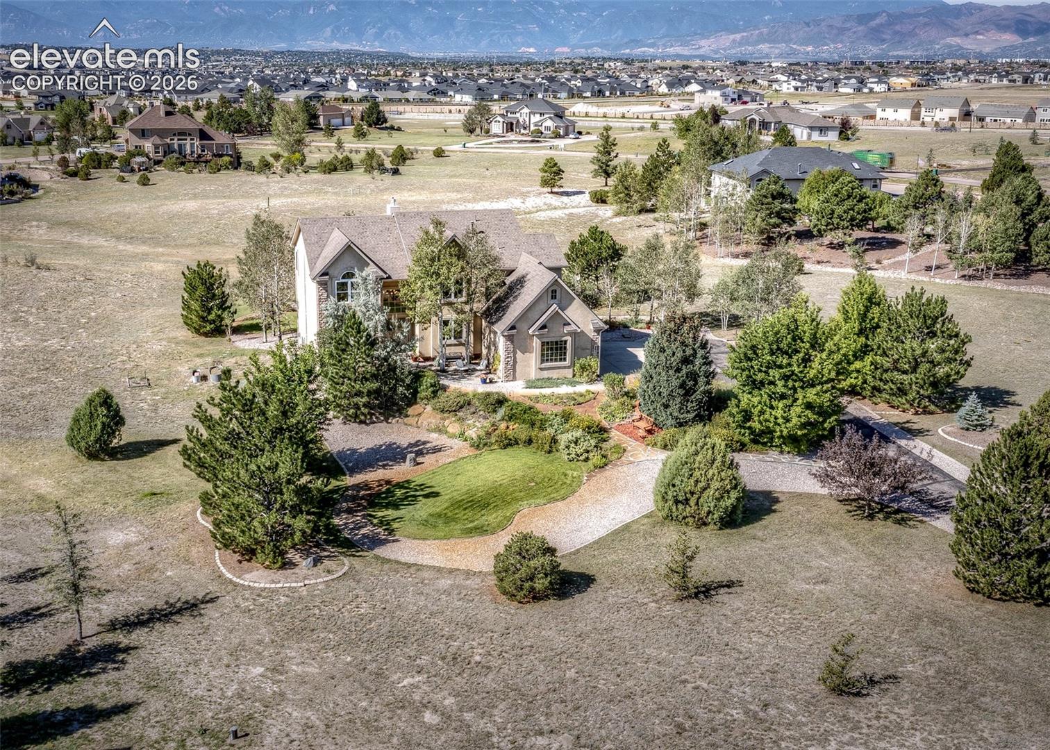 Expansive property featuring a stone and stucco exterior, multiple gables, a circular driveway, mature landscaping, and mountain backdrop