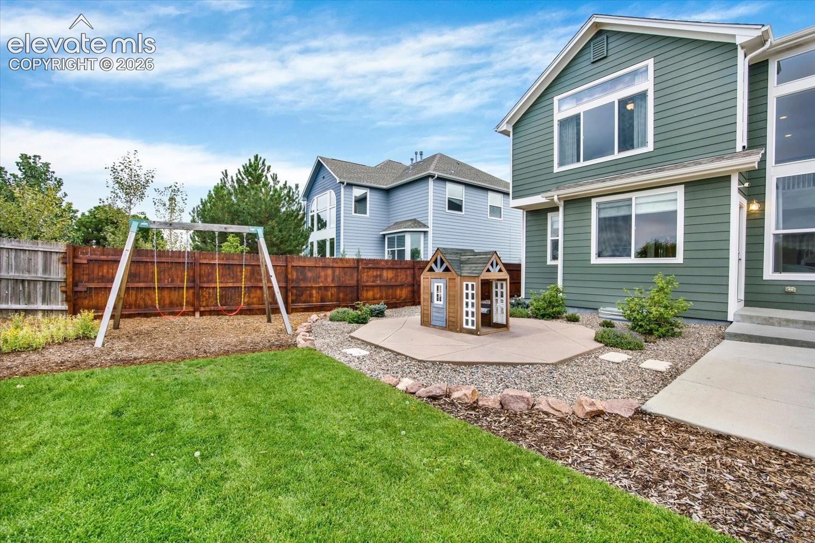 Fenced backyard featuring horizontal lap siding, an expansive manicured lawn, a concrete patio, and a stone-bordered landscaped area