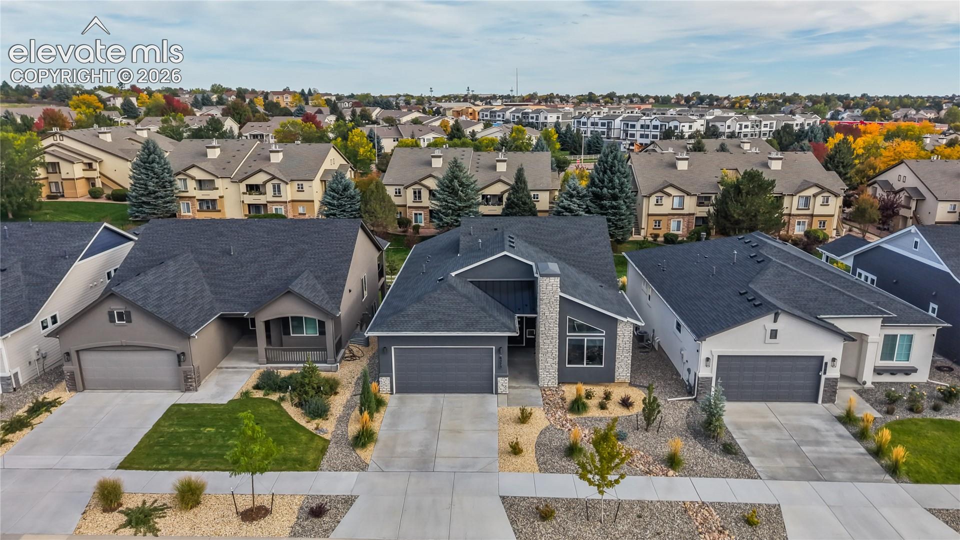 Aerial perspective featuring a single-story residence with a multi-gabled dark shingle roof, stone veneer exterior accents, two-car garage, and low-maintenance landscaping with rock mulch beds