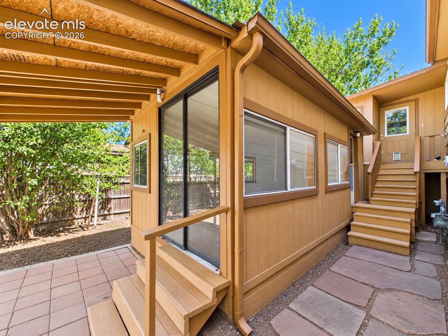 Exterior view highlights the enclosed sunroom addition with multiple windows, screened access, and adjacent paved outdoor space.