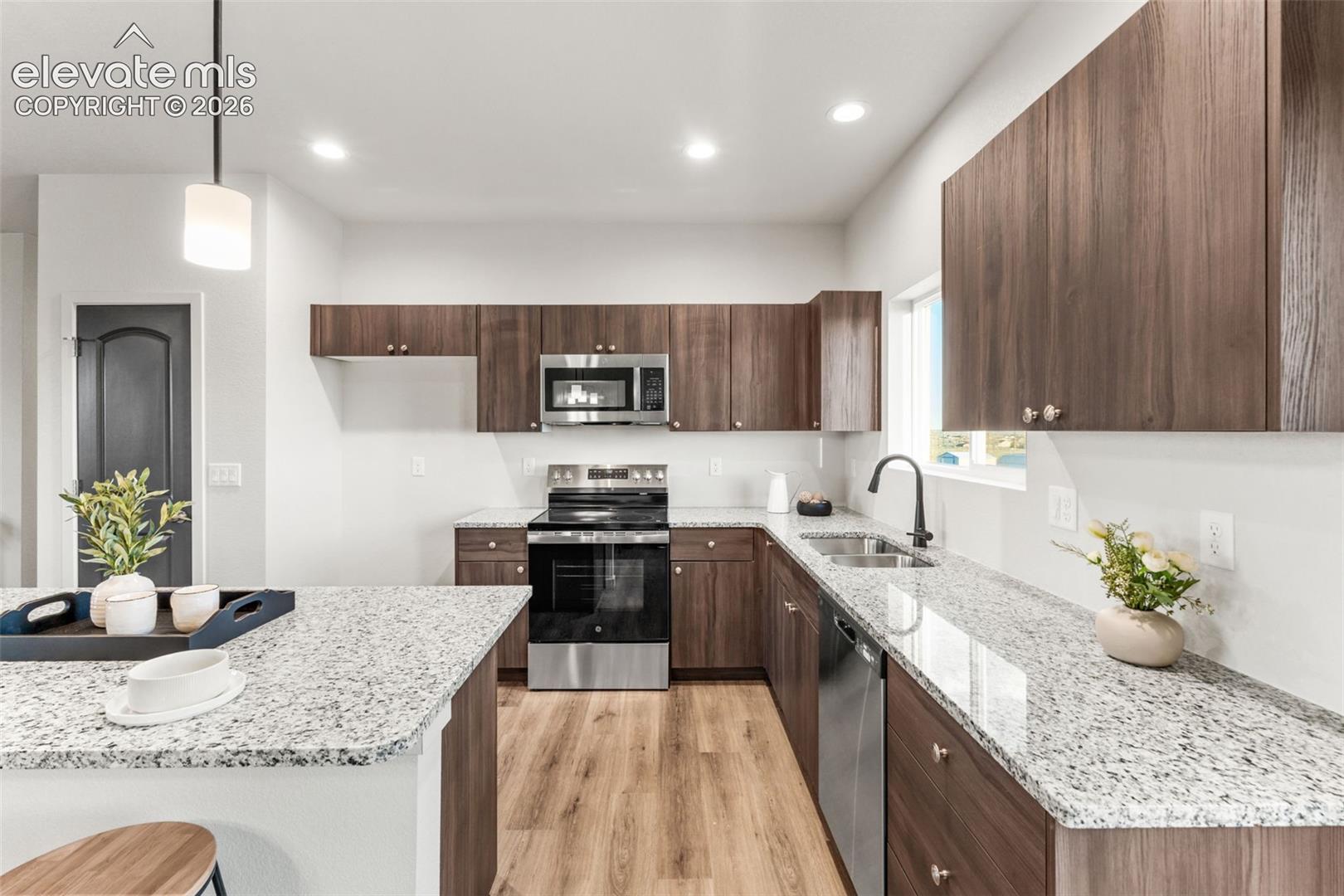Kitchen featuring wood-finish cabinetry, stone-surface countertops, stainless steel appliances, wood-finish flooring, and a pendant light fixture