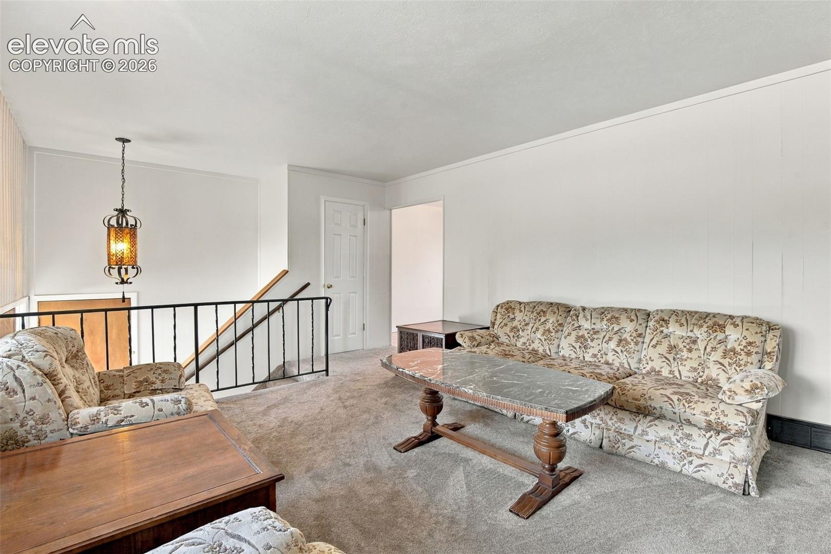 Neutral-toned interior space featuring carpeted flooring, paneled walls, a metal railing, and an ornate metal pendant light fixture