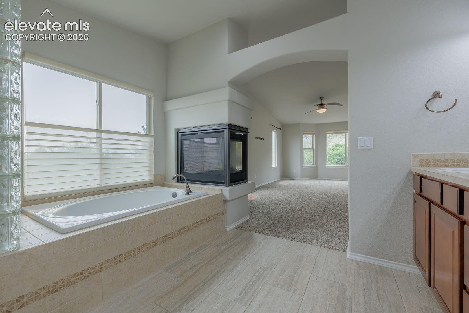 Soaking tub with tile surround, glass block partition, and an adjacent two-sided fireplace
