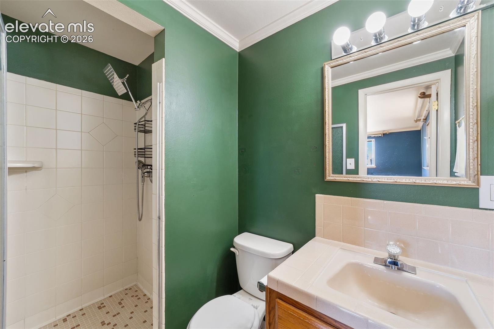 Bathroom featuring a white tile shower with mosaic floor, a vanity with an integrated sink, a rectangular framed mirror, and a three-light fixture