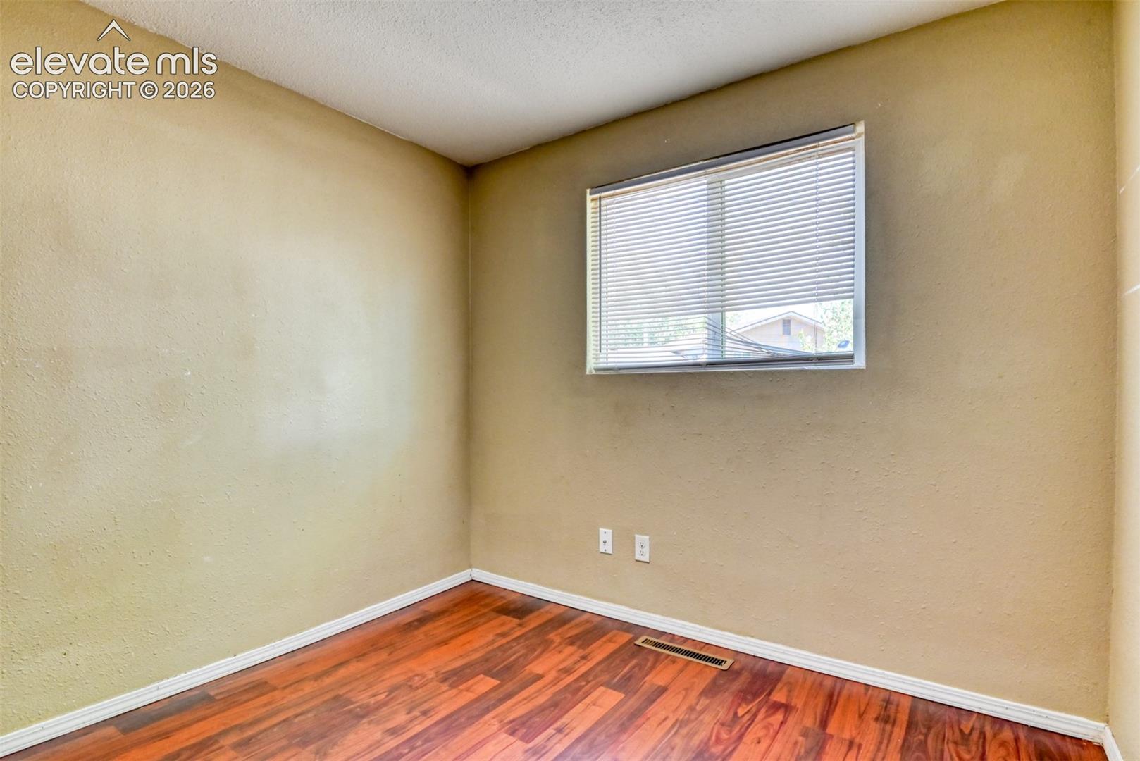 Interior room featuring wood-finish flooring, light-colored walls, and a window with horizontal blinds