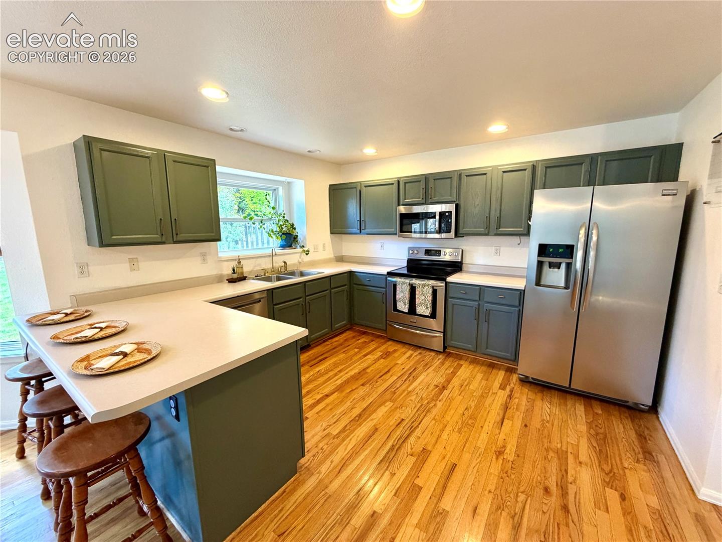 Kitchen featuring a breakfast bar, wood-finish flooring, dark green cabinetry, light countertops, and stainless steel appliances