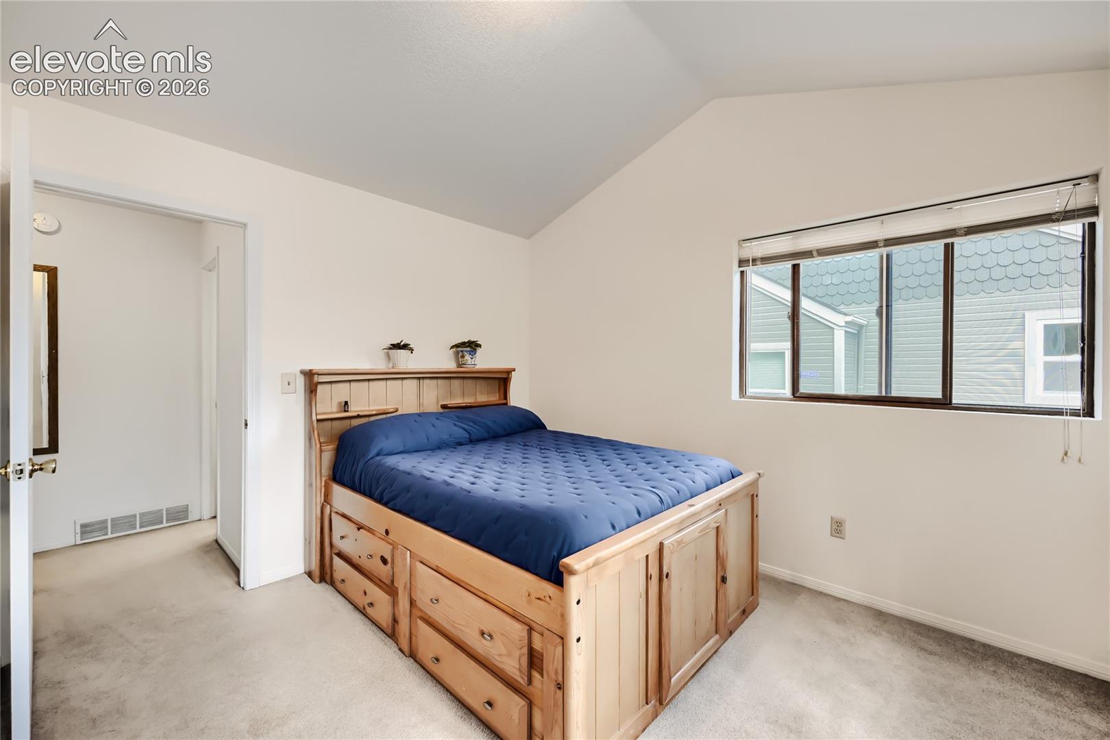 Vaulted ceiling, wall-to-wall carpeting, and a window with blinds