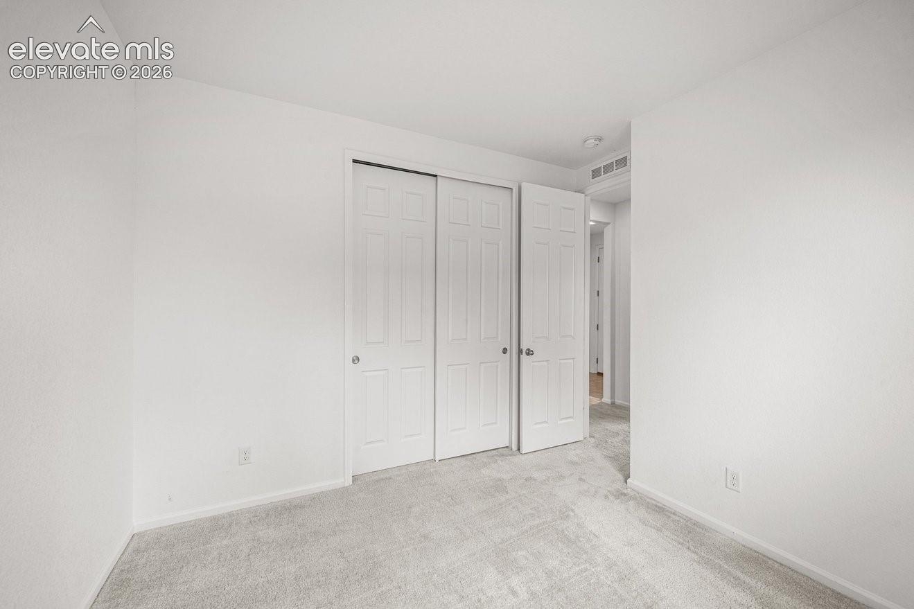 Spacious bedroom featuring triple-panel closet doors with vertical detailing, neutral carpet flooring, and pristine white walls with soft recessed lighting throughout