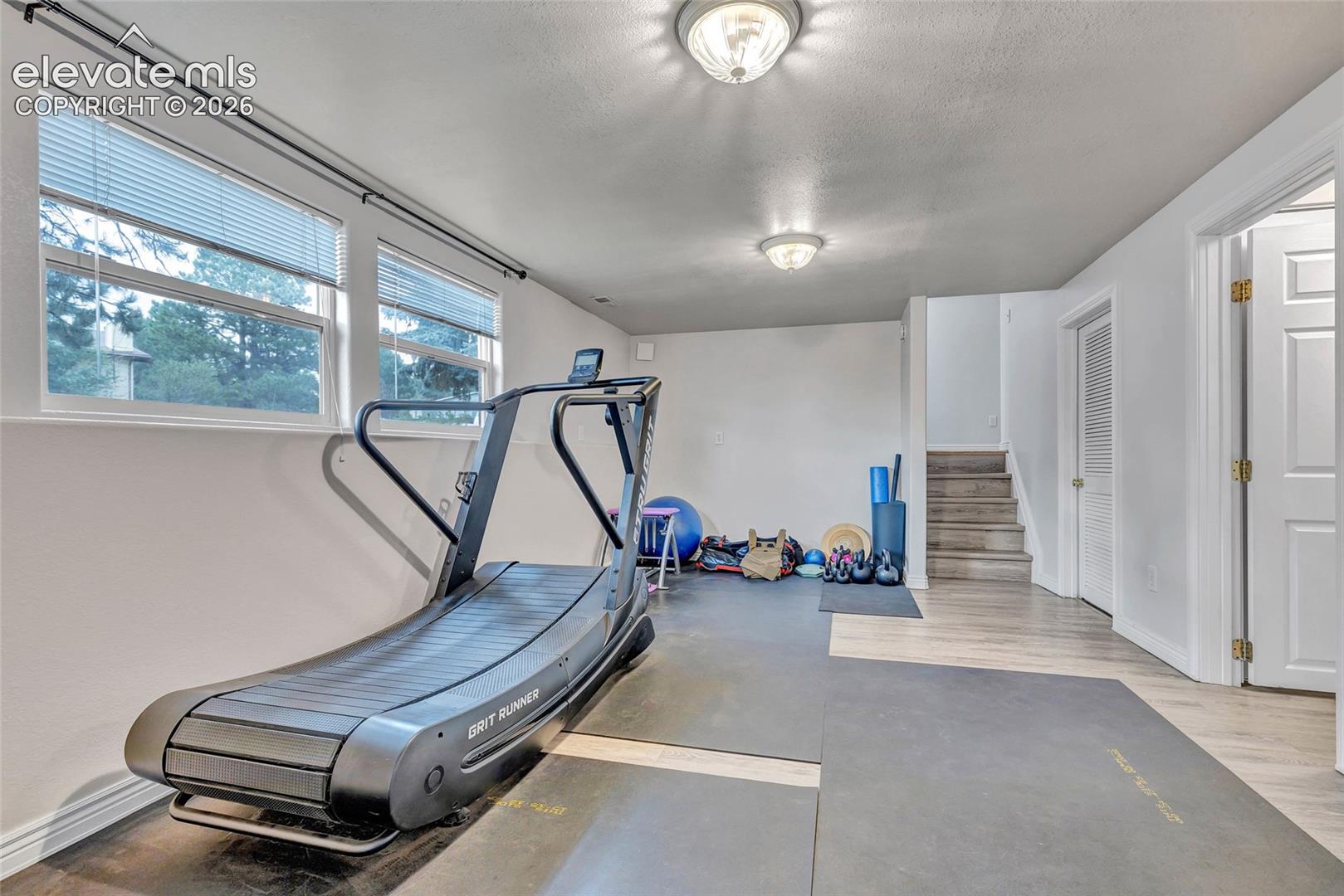 Spacious room featuring light wood-finish flooring, white walls, and multiple windows with blinds