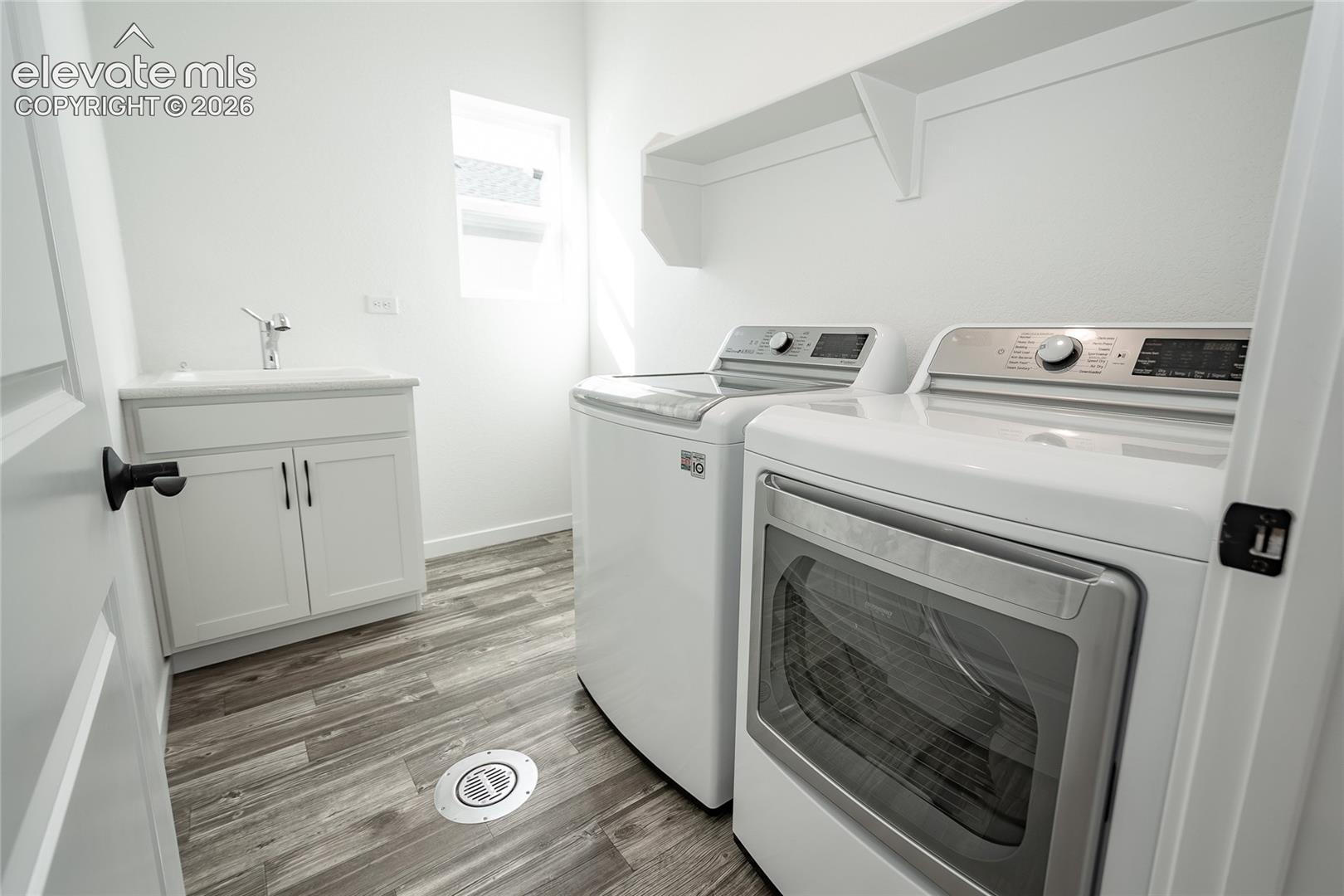 Utility room featuring a white vanity with a composite countertop and integrated sink, wood-finish flooring, and built-in upper shelving