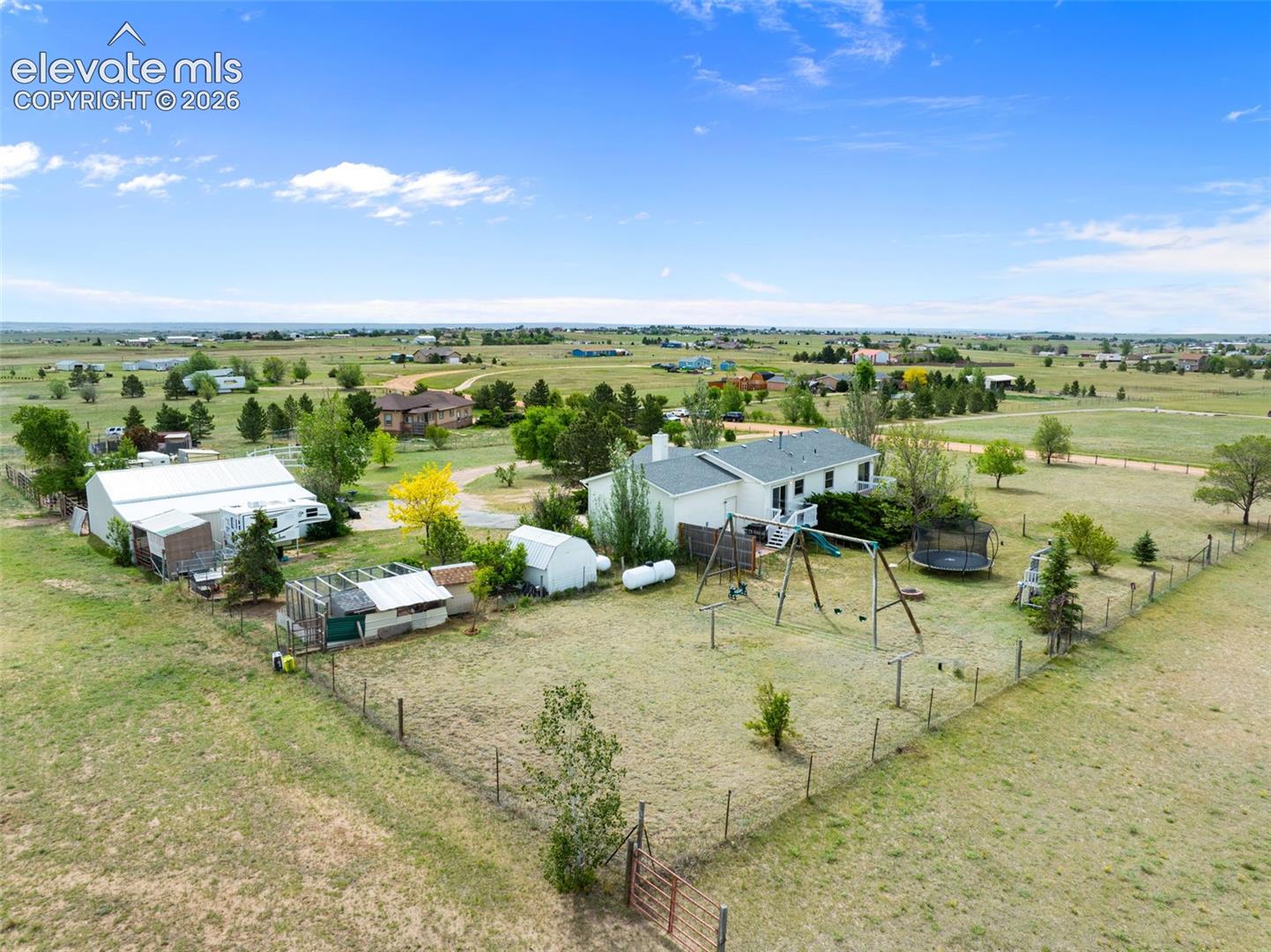 Expansive rural property featuring a white residence with a dark roof, multiple outbuildings, and extensive open land