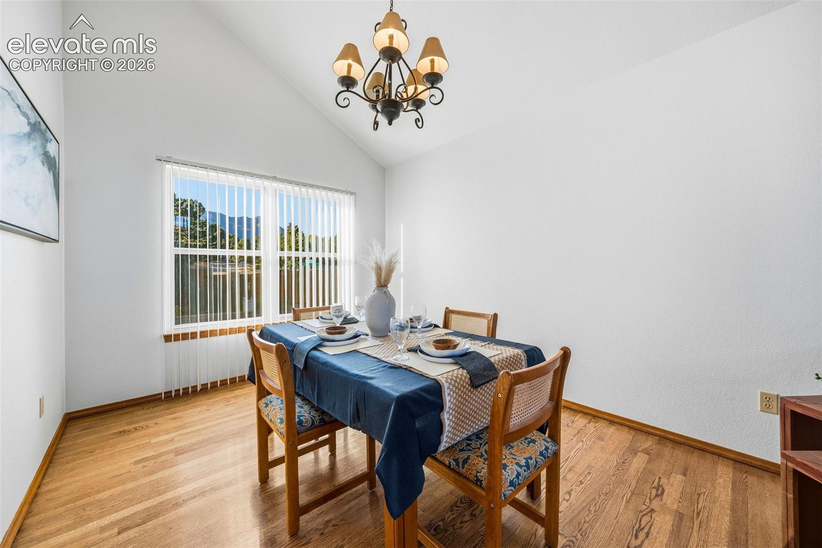Vaulted ceiling, wood-finish flooring, and multi-light chandelier
