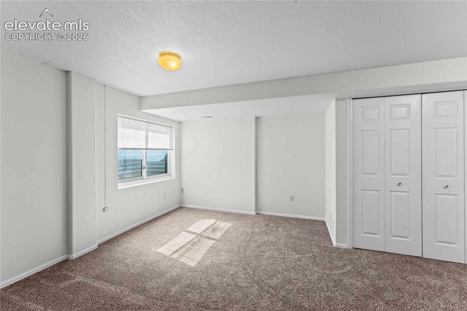 Neutral wall paint throughout, carpeted flooring, window with blinds, and built-in closet with bi-fold doors