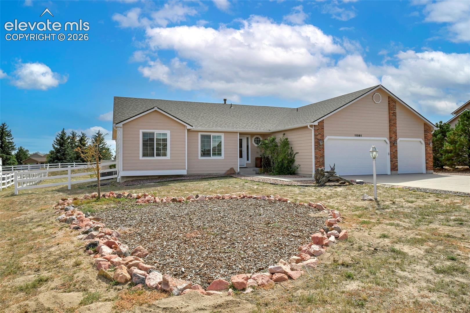 Ranch-style residence featuring a three-car garage, white fencing, and a decorative rock garden