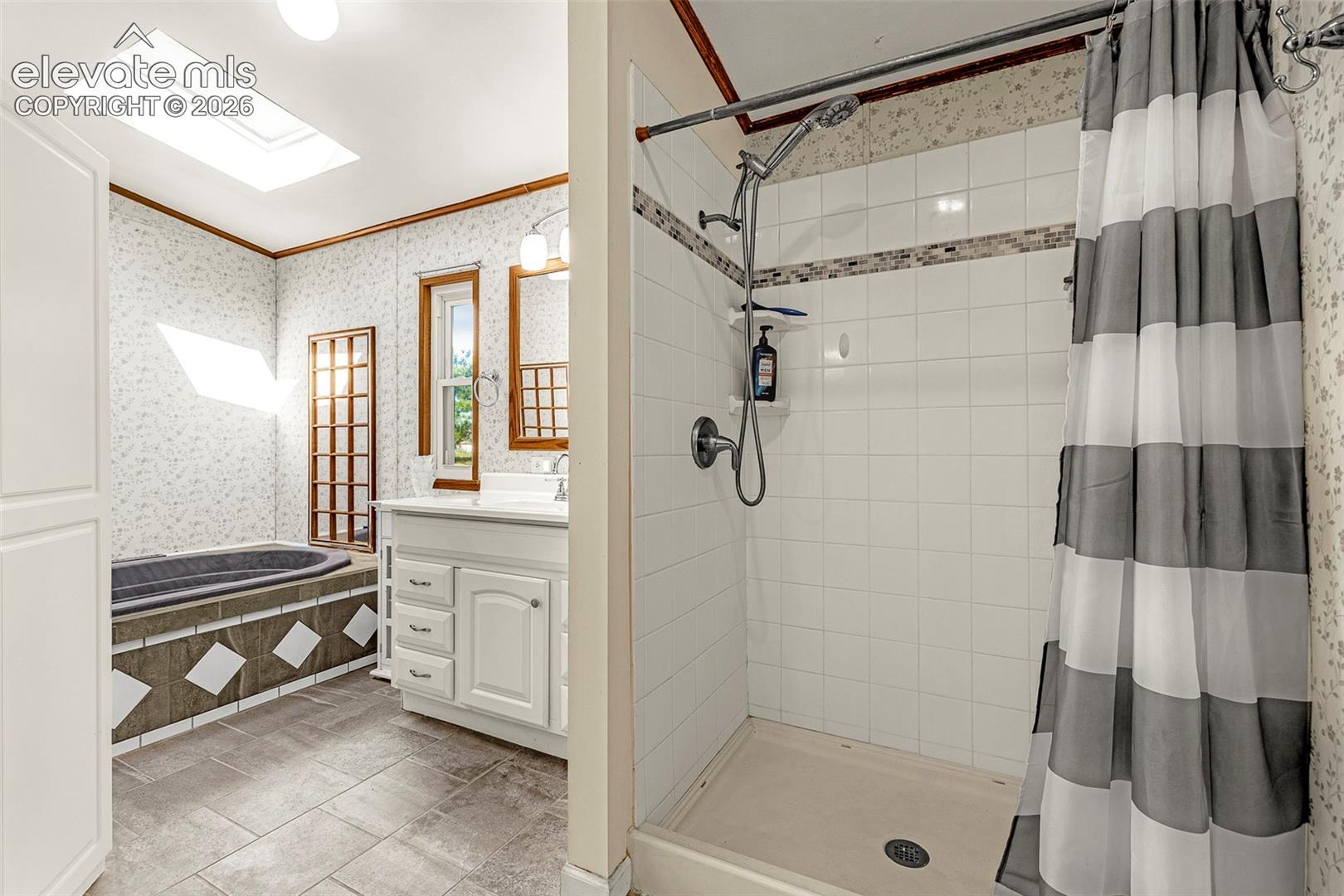 Bathroom featuring a tile-surround bathtub, a white vanity with integrated cabinetry, a standalone shower with tiled walls, a ceiling skylight, and large-format floor tiling