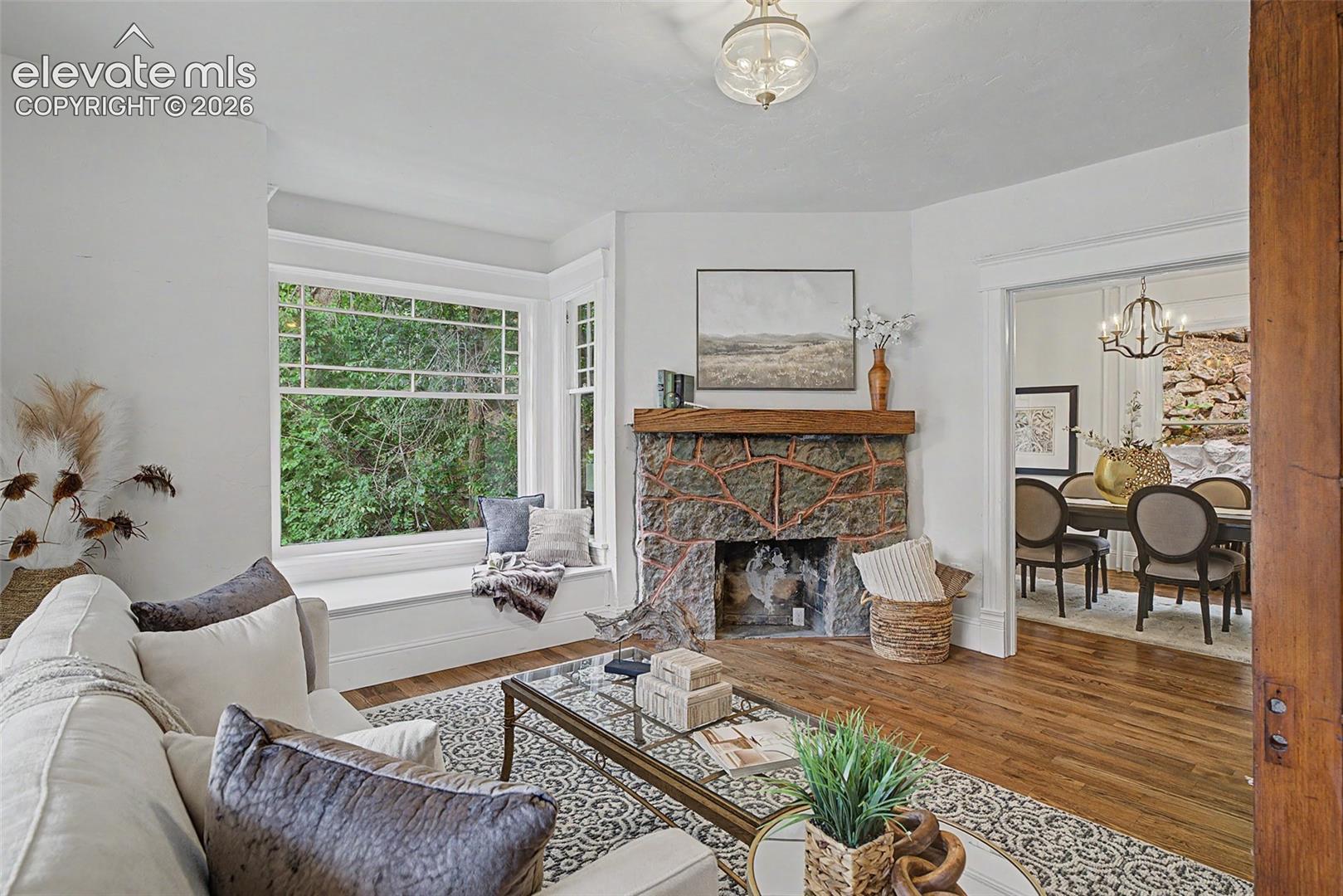Living area featuring a stone fireplace with a wood mantle, a spacious bay window with a window seat, and wood-finish flooring