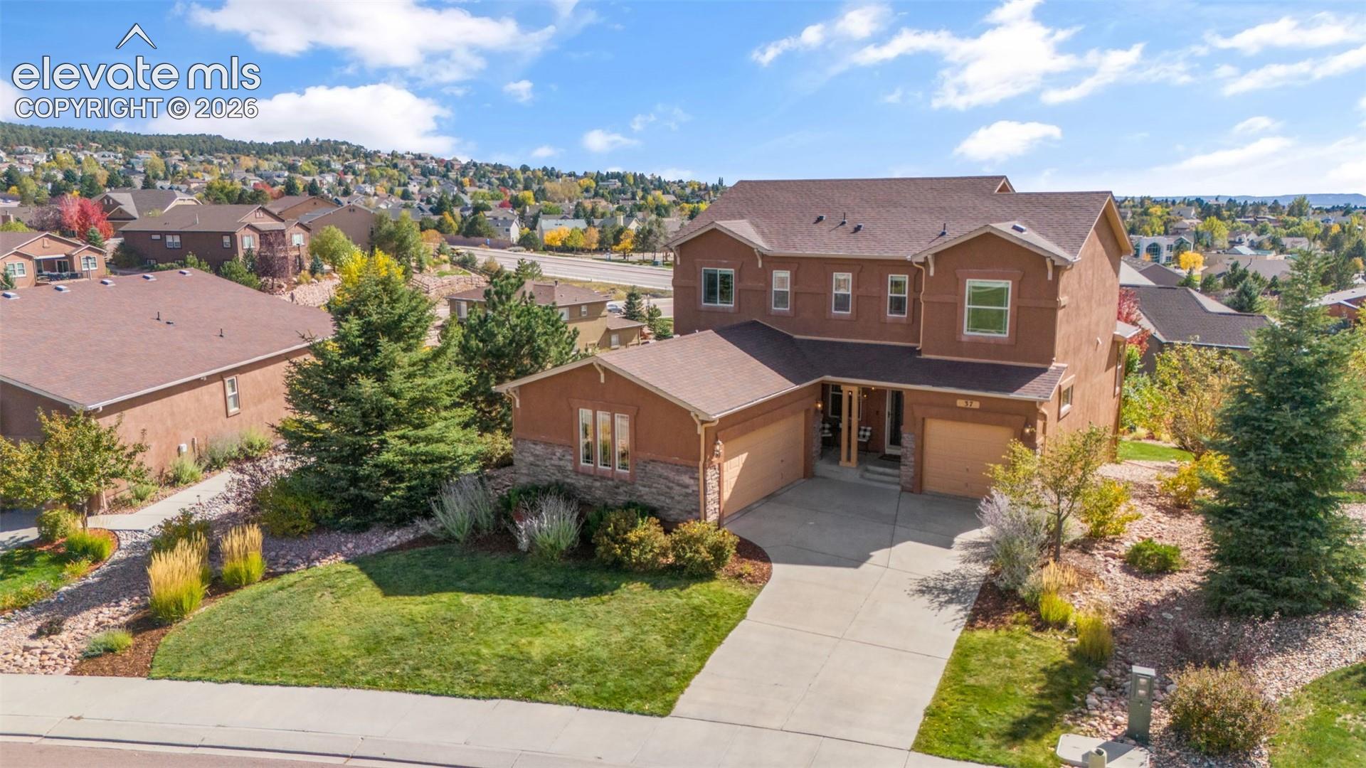 Two-story residence featuring stucco exterior, stone facade accents, shingled roof, attached three-car garage, and concrete driveway