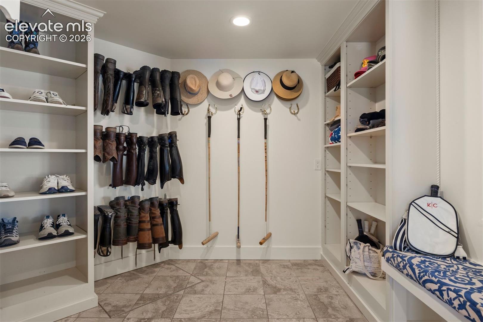 Spacious two-part mudroom room, thoughtfully outfitted as a true equestrian room with dedicated wall racks for tall boots and shoes, hat and coat hooks, and extensive built-in shelving.